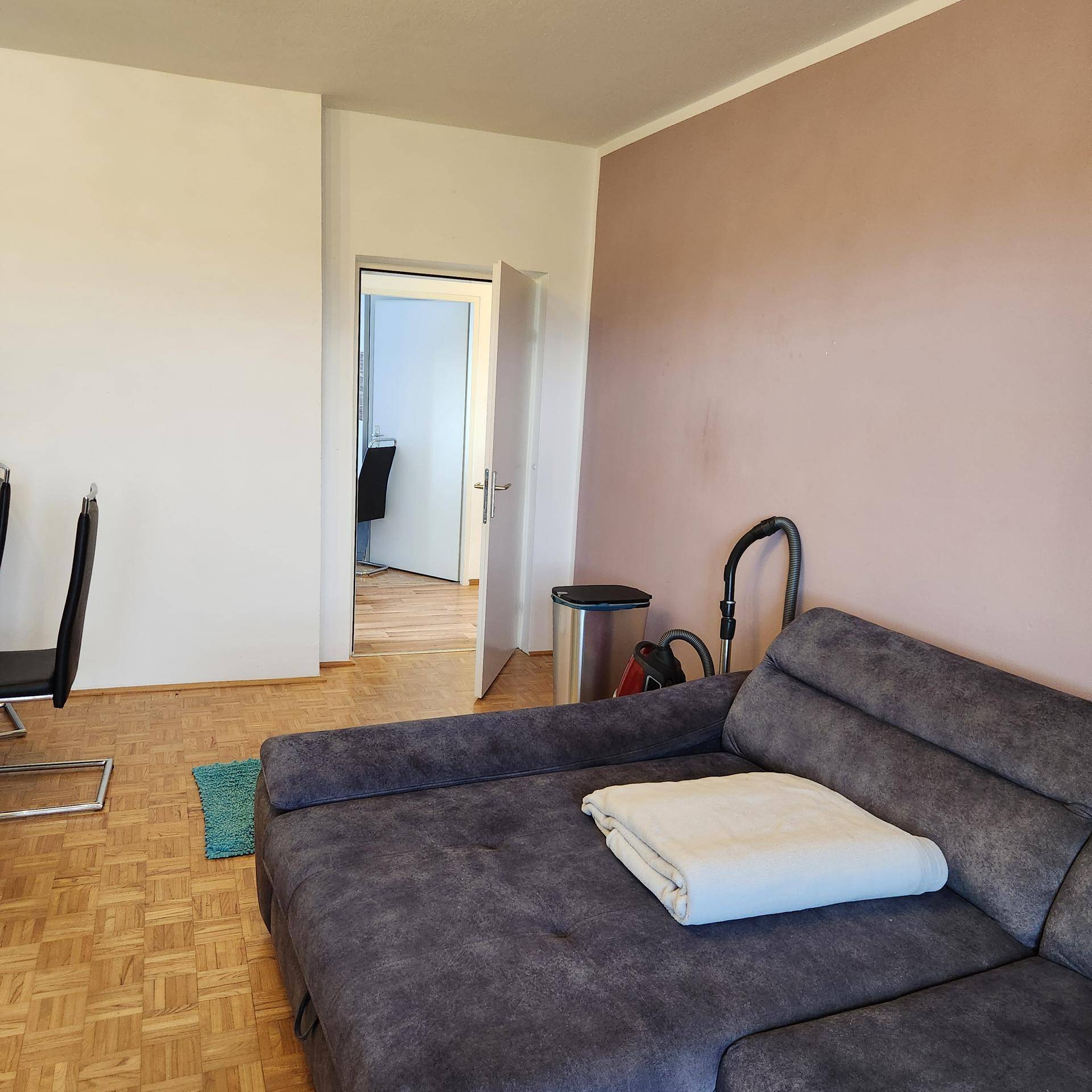 Teilansicht des Wohnzimmers mit grauem Sofa und Blick in einen angrenzenden Raum.