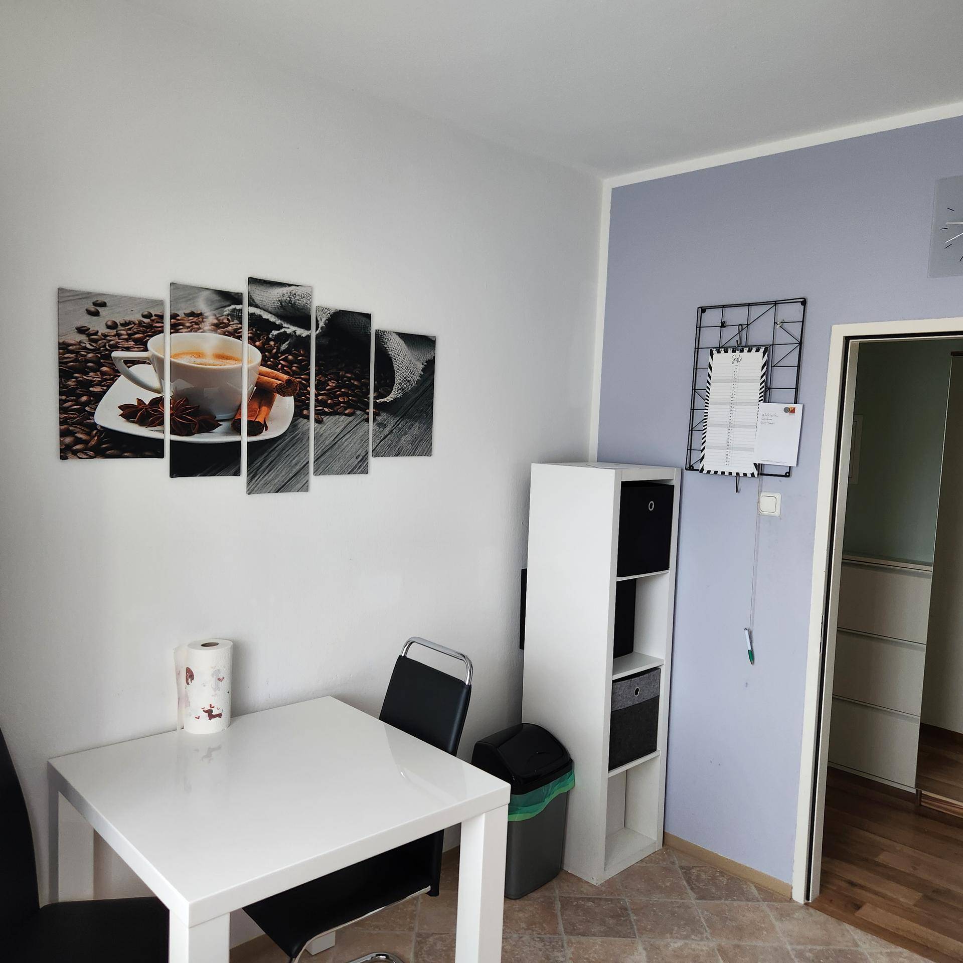 Essbereich mit weißem Tisch und Stühlen, dekoriert mit Kaffeebildern an der Wand.