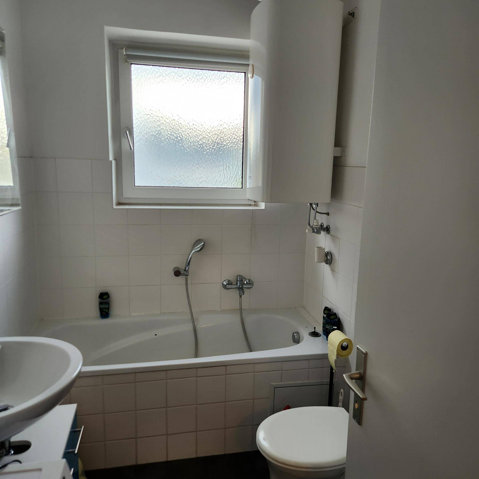 Helles Badezimmer mit Badewanne, WC, Waschbecken und einem Fenster für natürliche Belüftung.