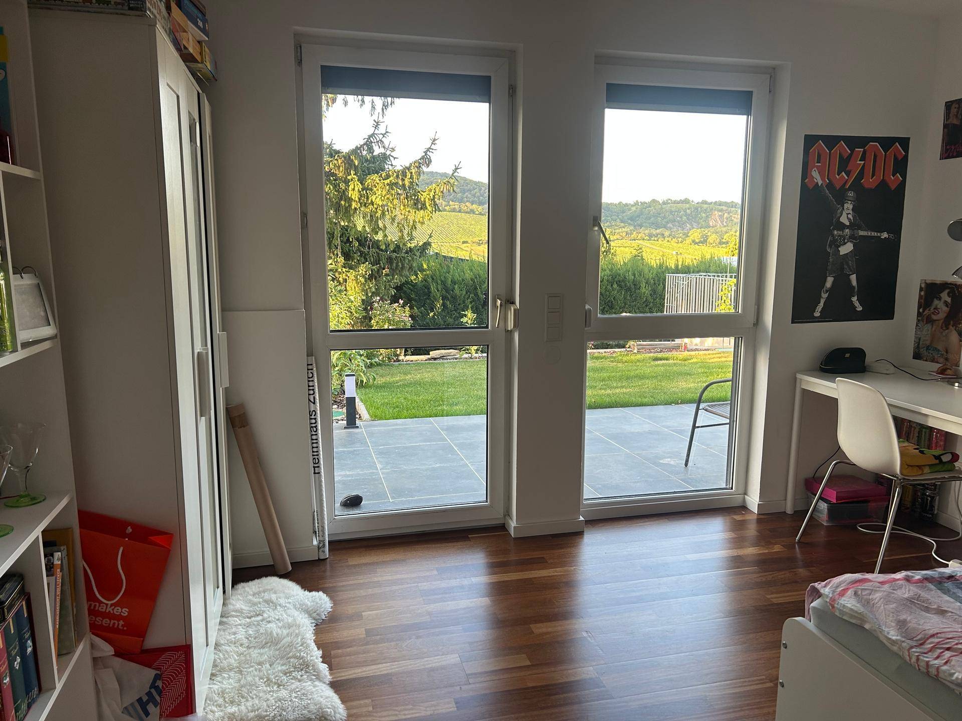 Helles Schlafzimmer mit Holzboden, Schreibtisch und direktem Zugang zur Terrasse.