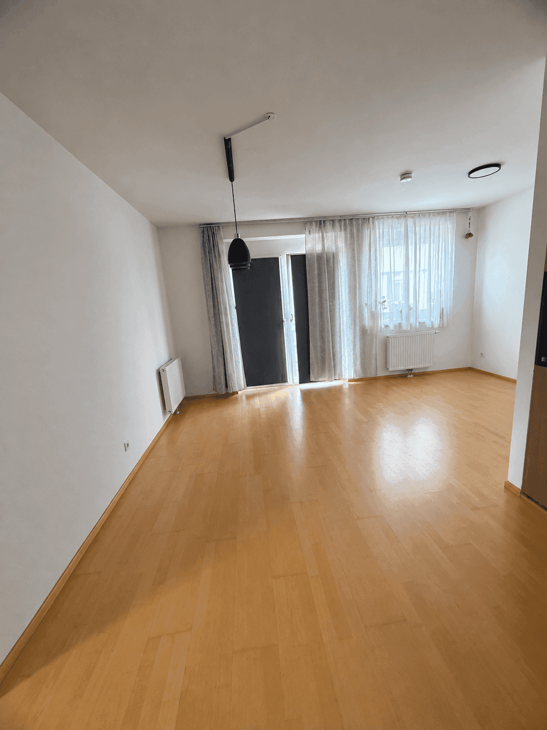 Helles Wohnzimmer mit hellem Parkettboden und Zugang zu einem Balkon oder einer Terrasse.