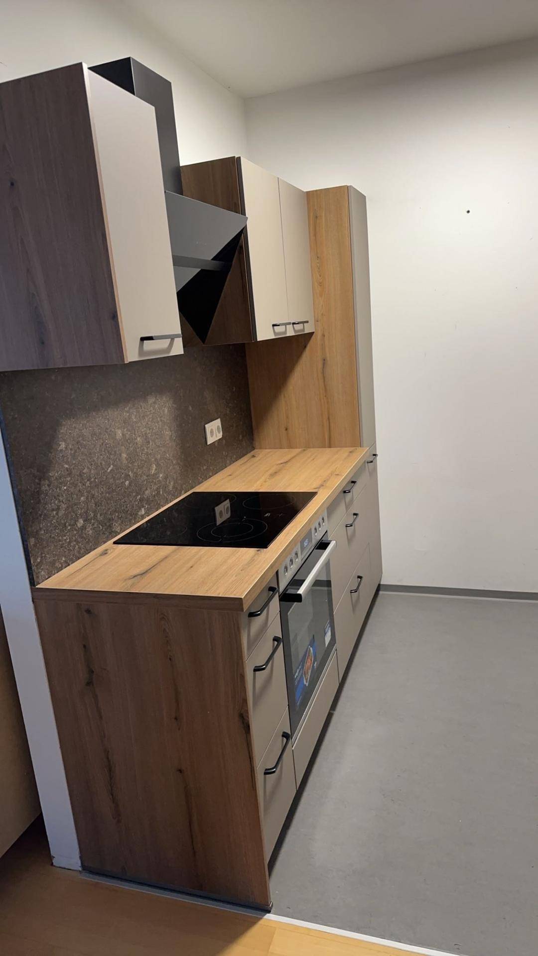 Moderne Küche mit Holz- und hellgrauen Schränken, Induktionskochfeld und Backofen.