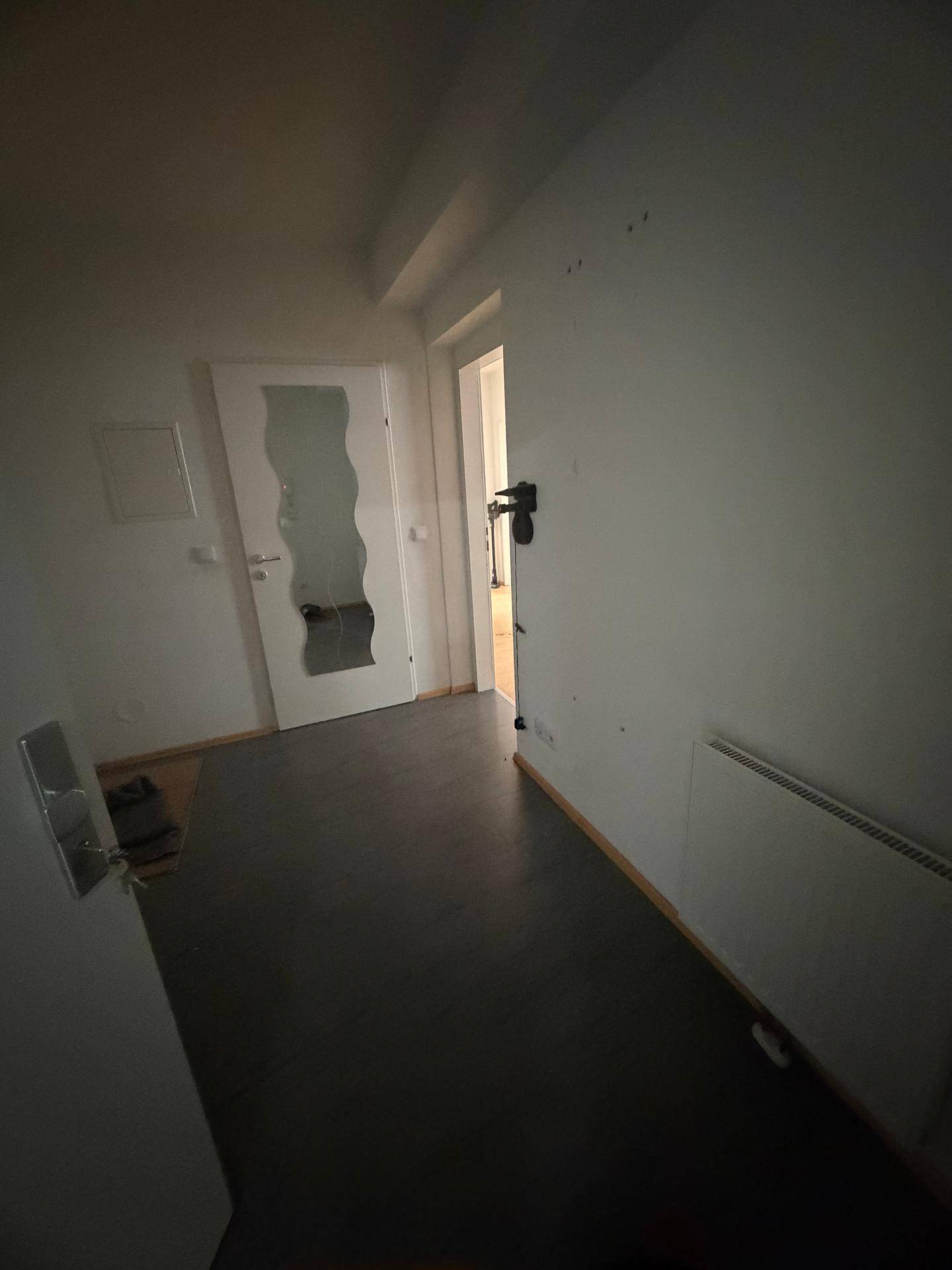 Dunkler Flur mit dunklem Boden und Heizkörper, der zu weiteren Räumen führt.