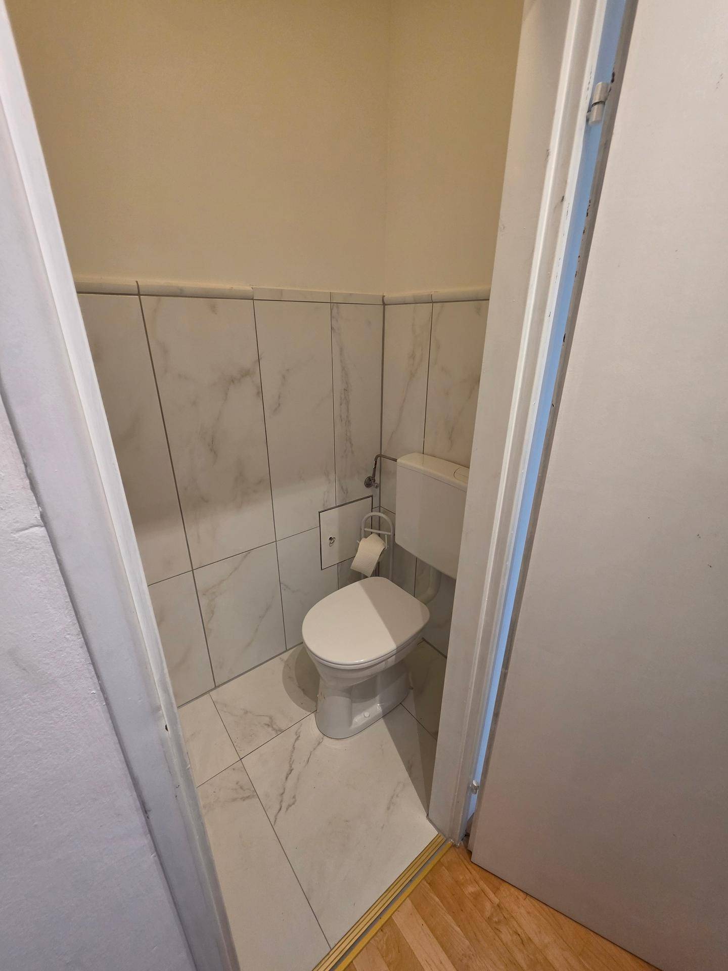 Separates Gäste-WC mit Wand-WC und hellen Fliesen.