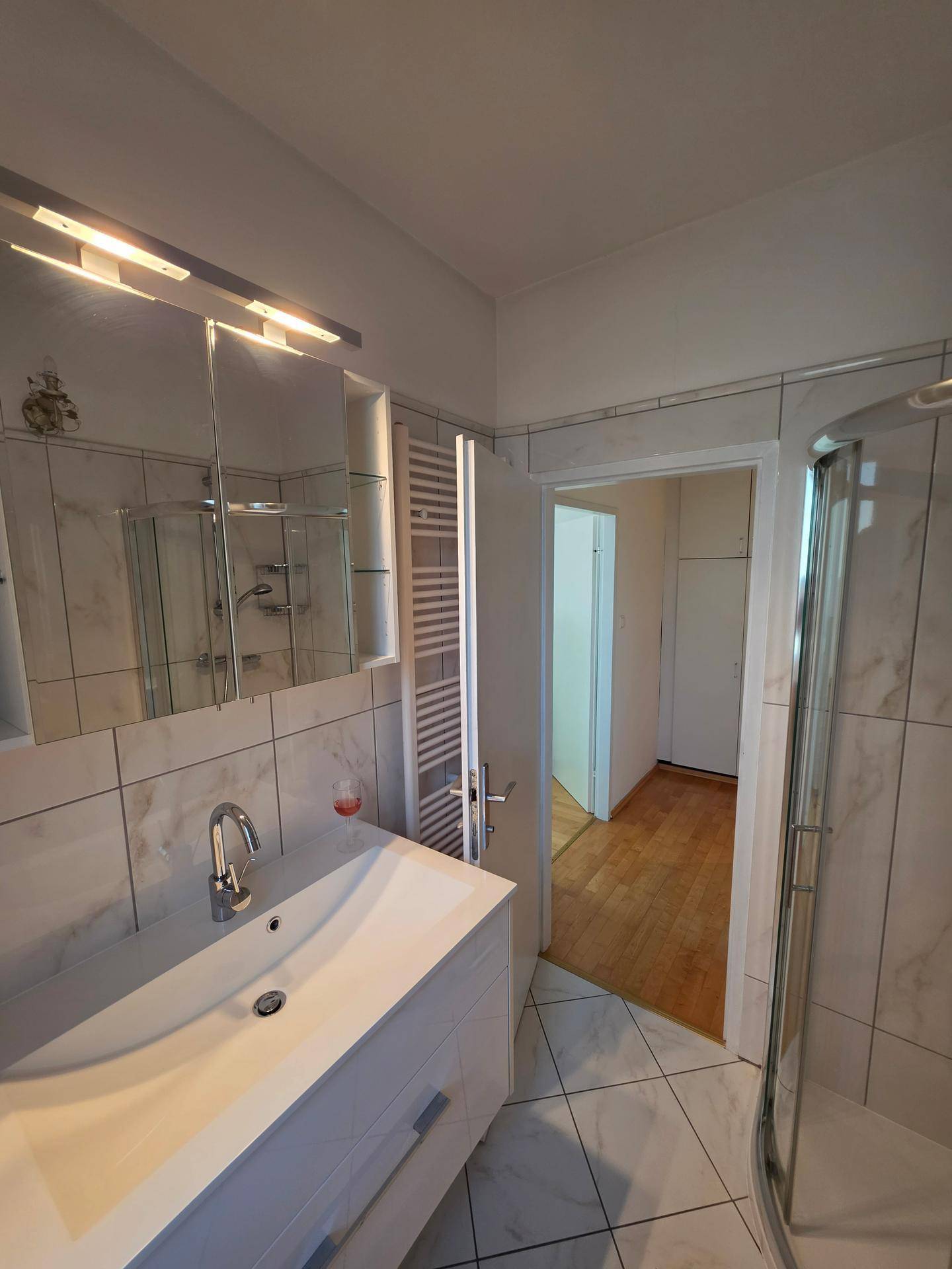 Badezimmer mit Waschtisch, Spiegelschrank und beheiztem Handtuchhalter.