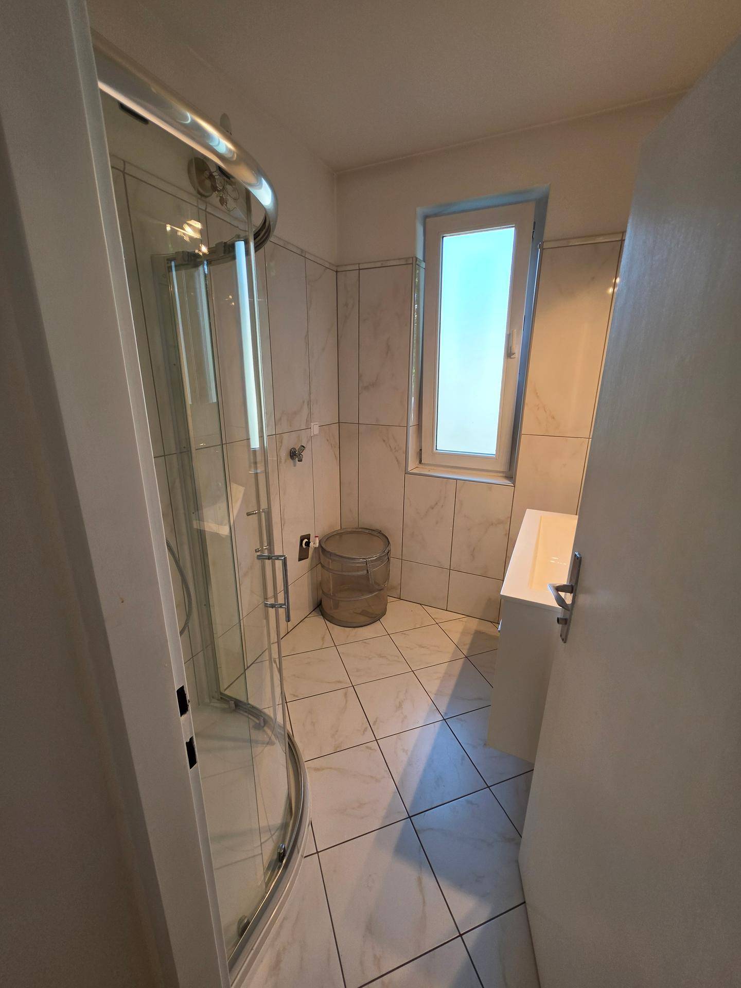 Modern gefliestes Badezimmer mit Duschkabine und Fenster für Tageslicht.