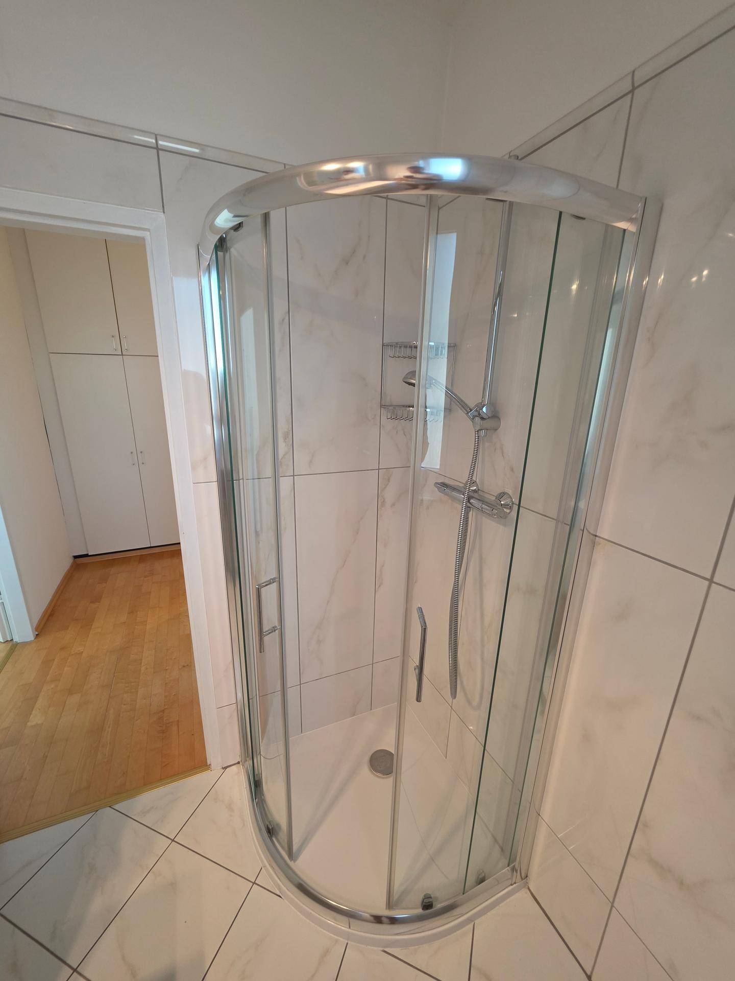 Geflieste Duschkabine mit Glastüren in einem hellen Badezimmer.