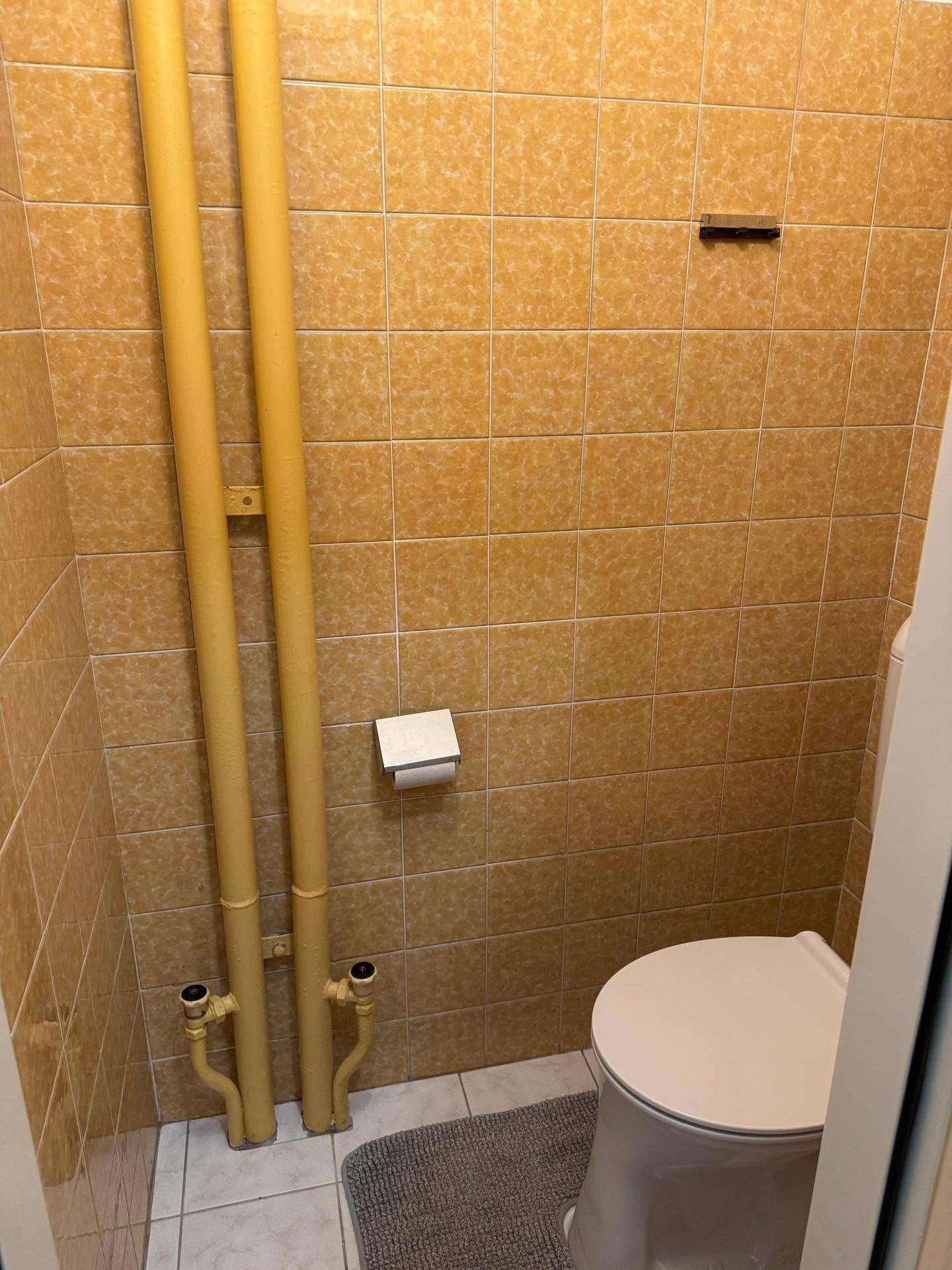 Kleines WC mit orangefarbenen Fliesen, Toilette und sichtbaren Rohren.