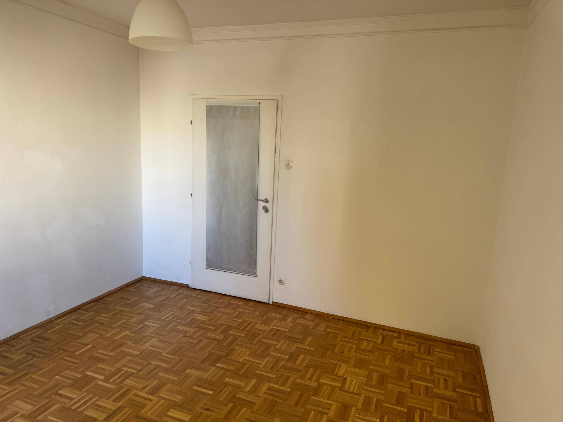 Leerer Raum mit Parkettboden und einer Tür mit Milchglas.