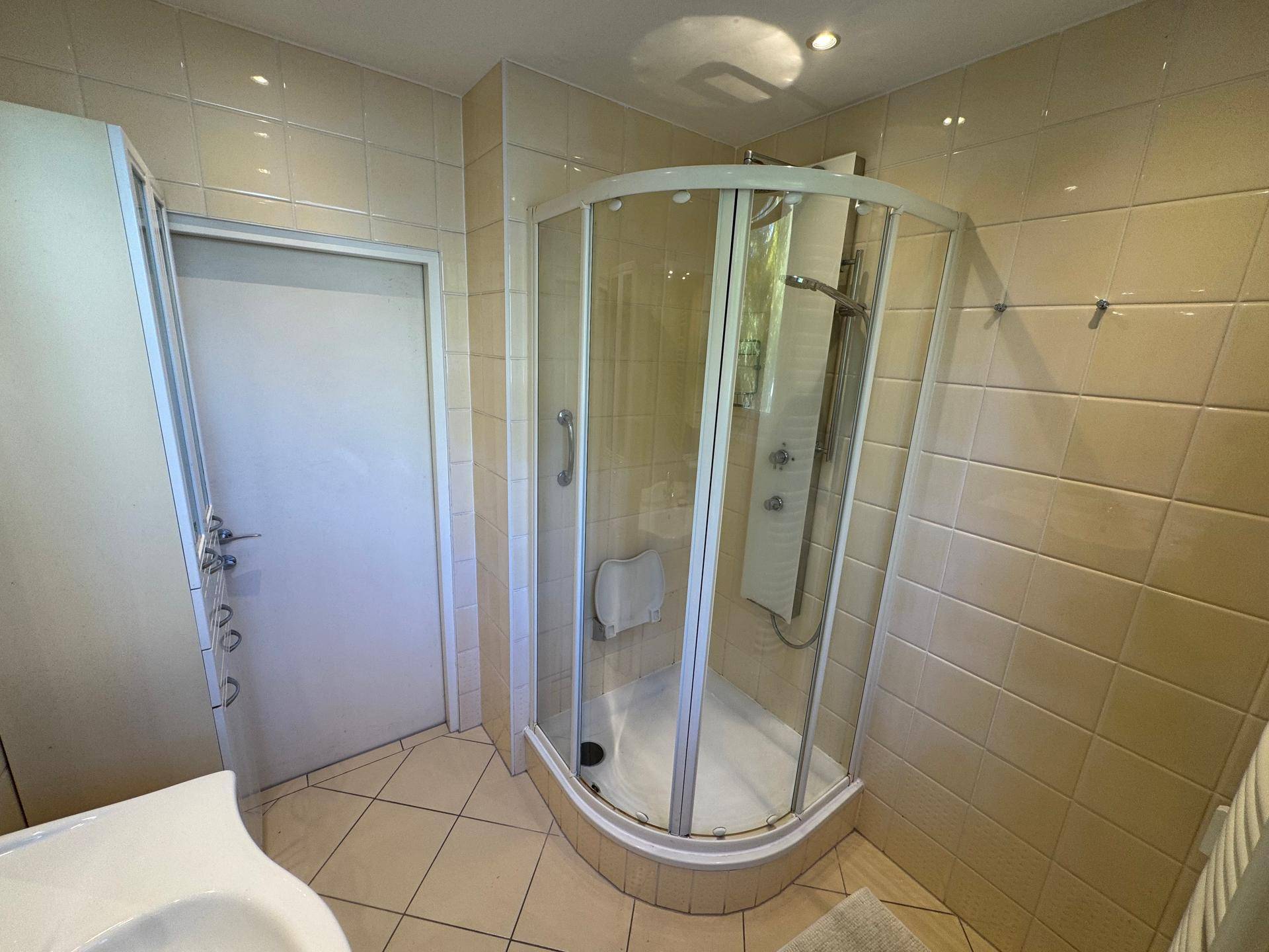 Duschkabine und Waschbecken in einem funktionalen Badezimmer mit beigen Fliesen.