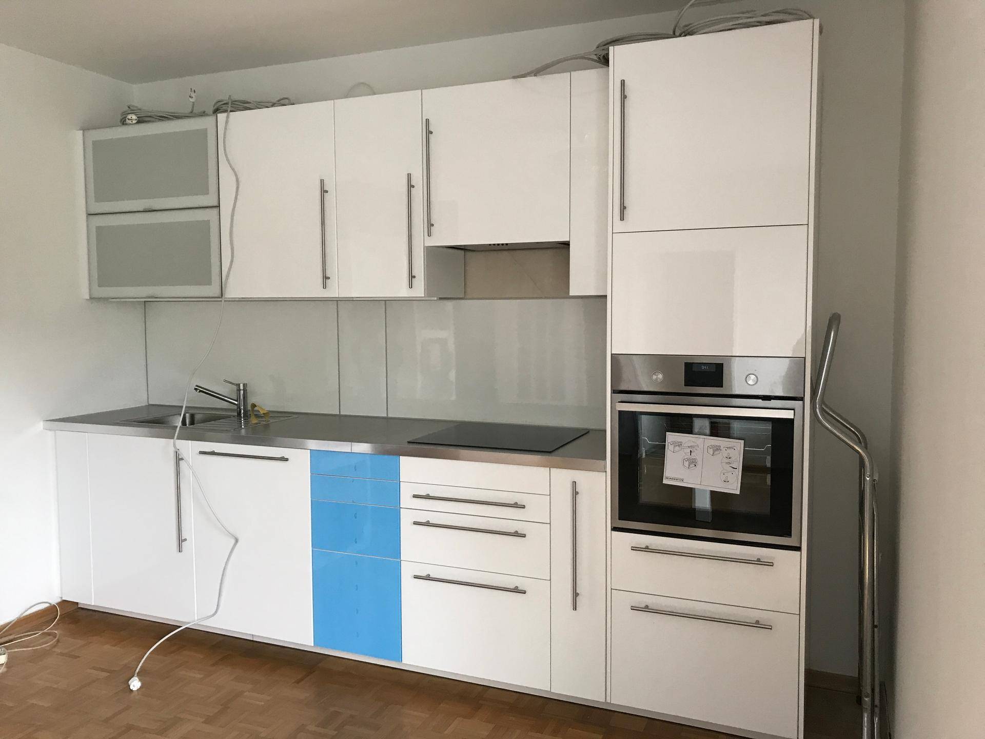 Moderne Einbauküche mit weißen Hochglanzfronten, integriertem Backofen und blauen Akzenten.
