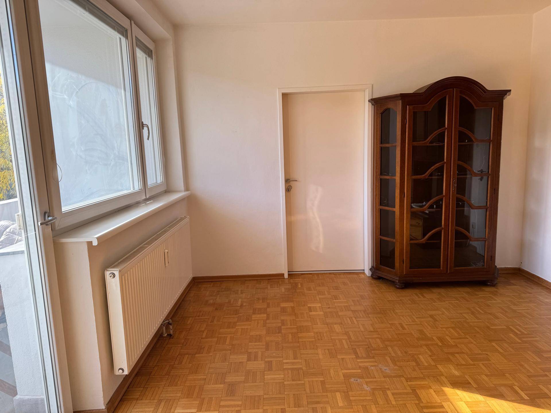 Leerer Raum mit Parkettboden, großem Fenster und Zugang zu einem Außenbereich.