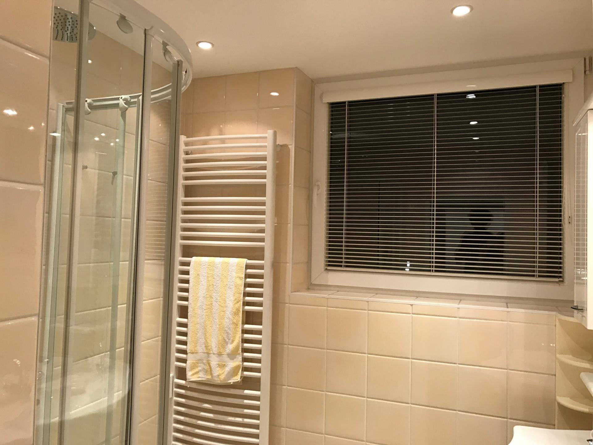Modernes Badezimmer mit beigefarbenen Fliesen, Duschkabine, Fenster und beheiztem Handtuchhalter.