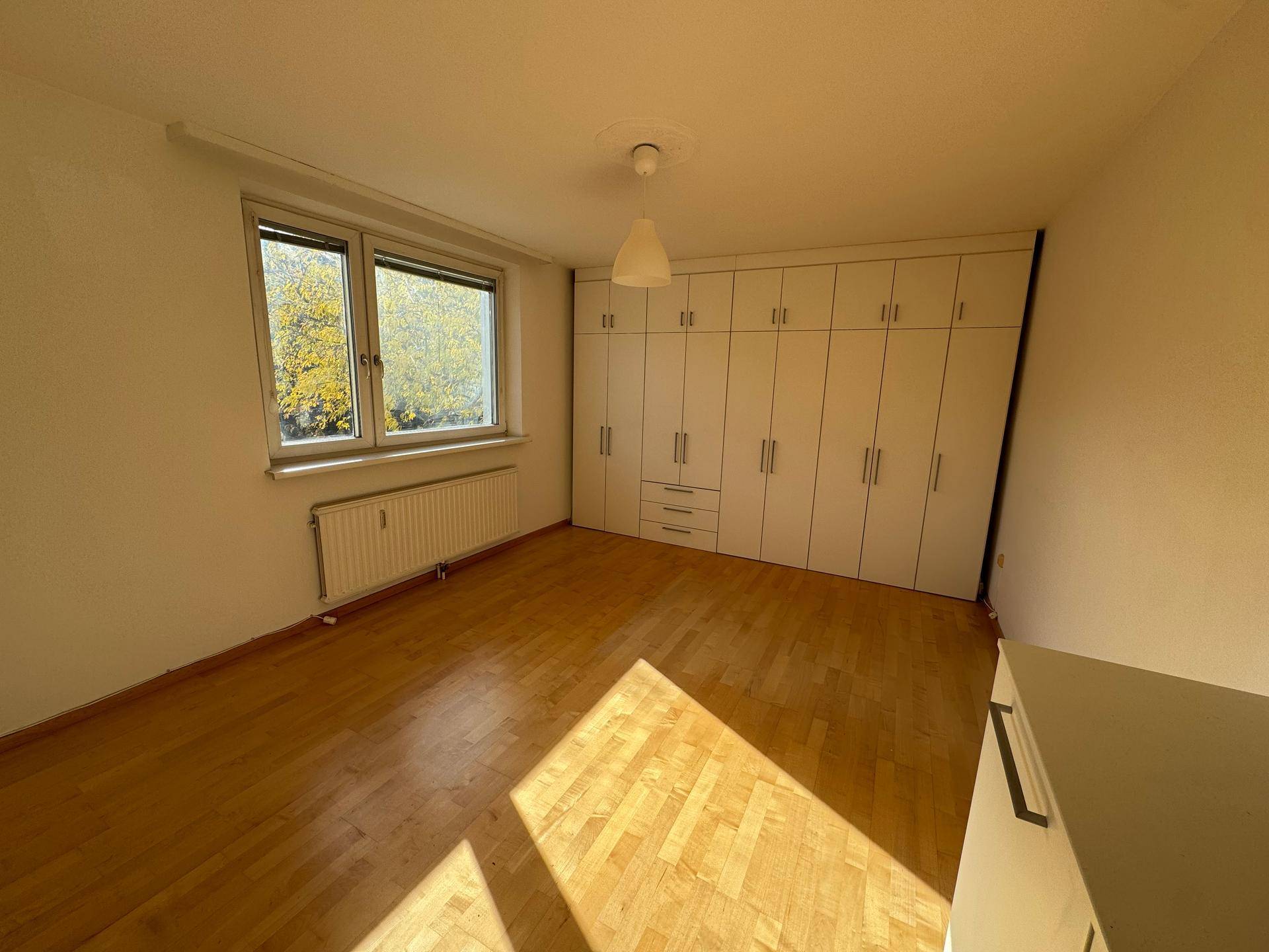 Helles Schlafzimmer mit Einbauschränken, Parkettboden und Fenster mit Blick ins Grüne.