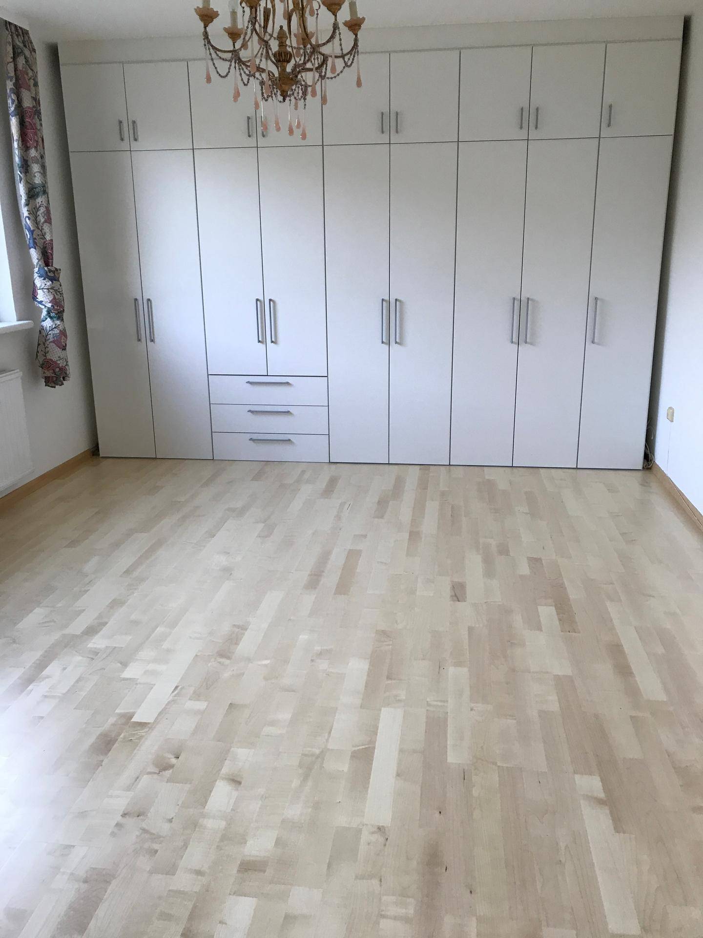 Geräumiges Schlafzimmer mit großem Einbauschrank, hellem Parkettboden und Kronleuchter.