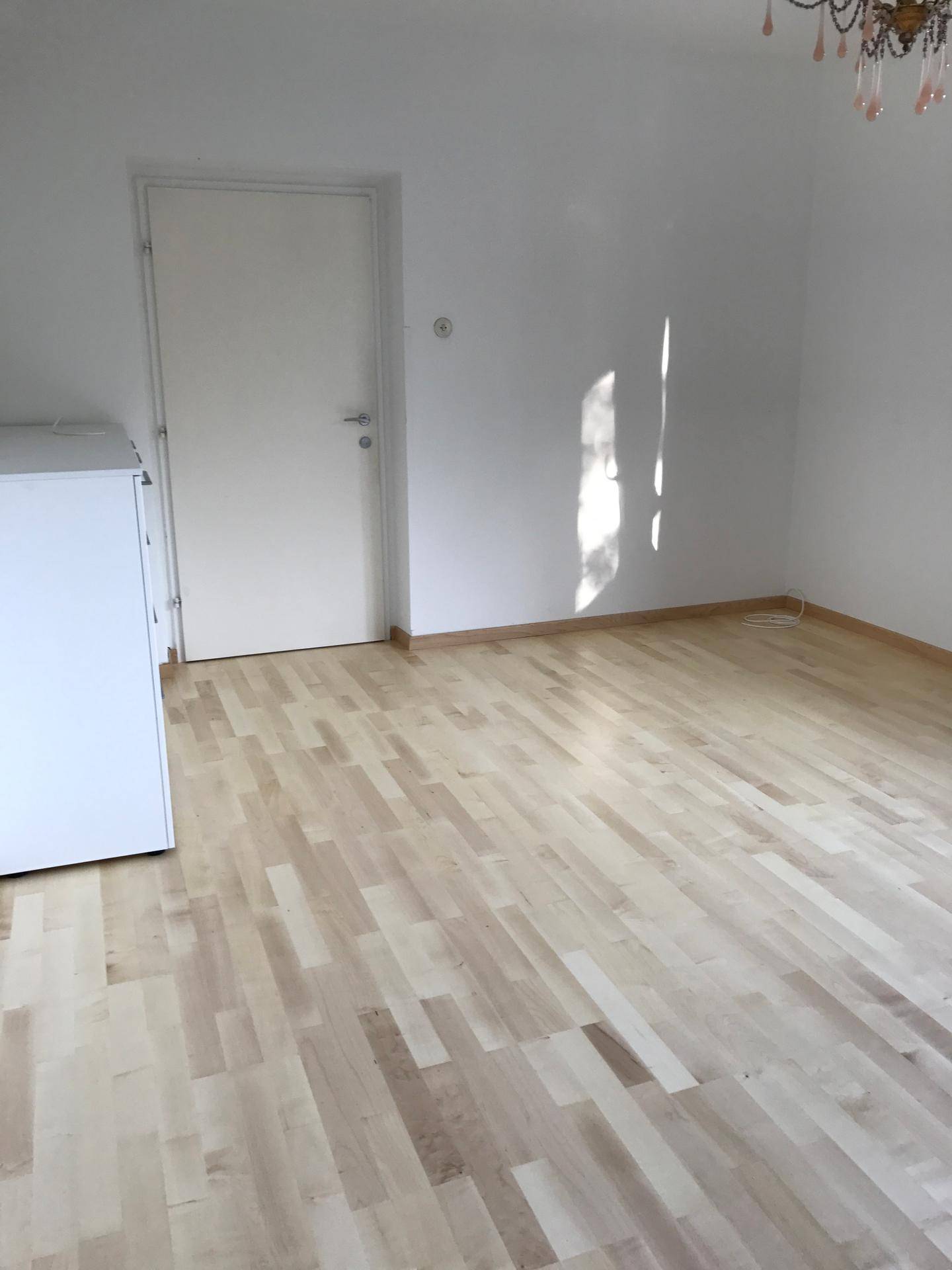 Leerer Raum mit hellem Holzparkettboden und weiß gestrichenen Wänden, sonnendurchflutet.