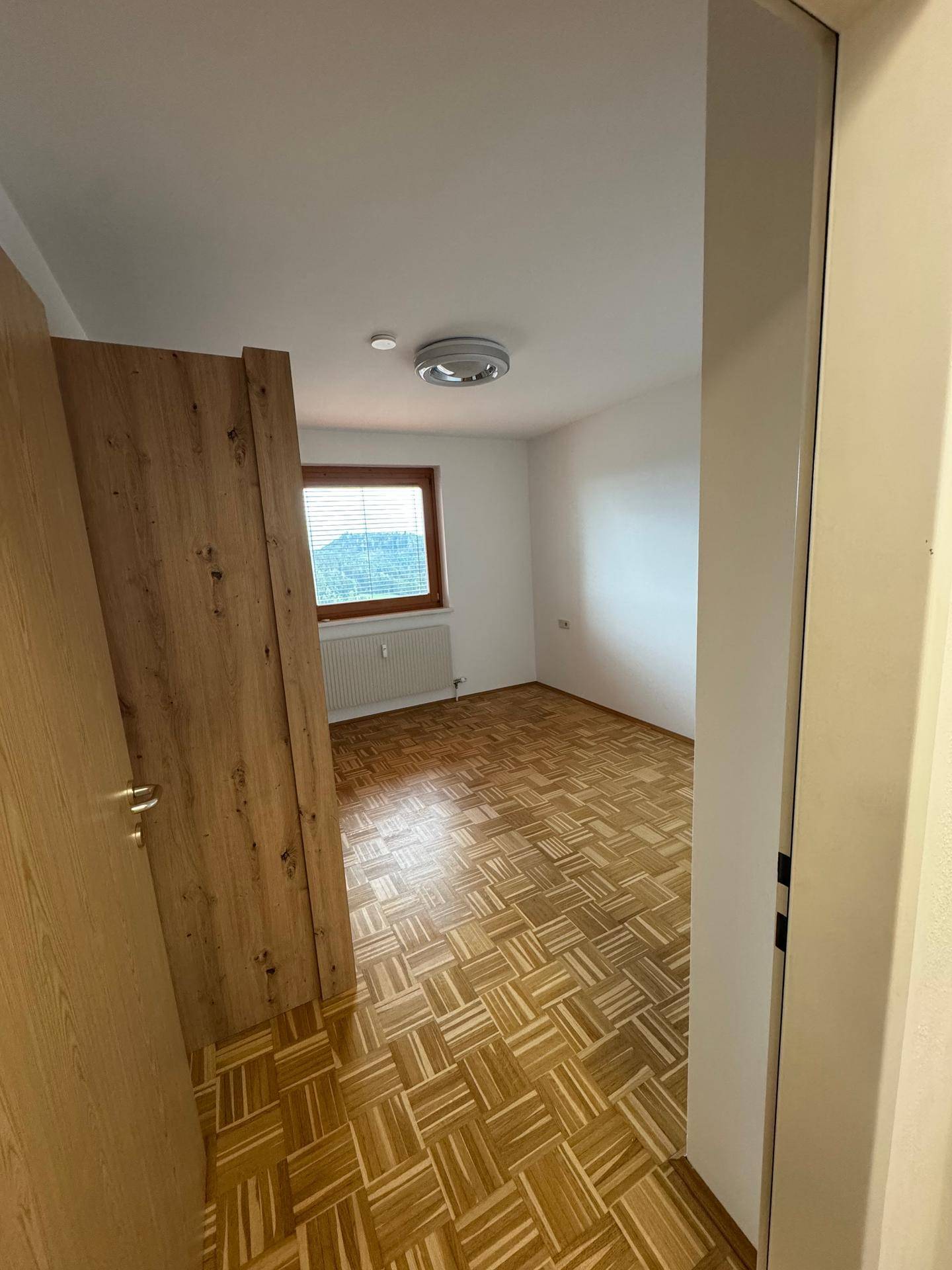 Geräumiges Schlafzimmer mit Parkettboden, weiß gestrichenen Wänden und Fenster mit Ausblick.