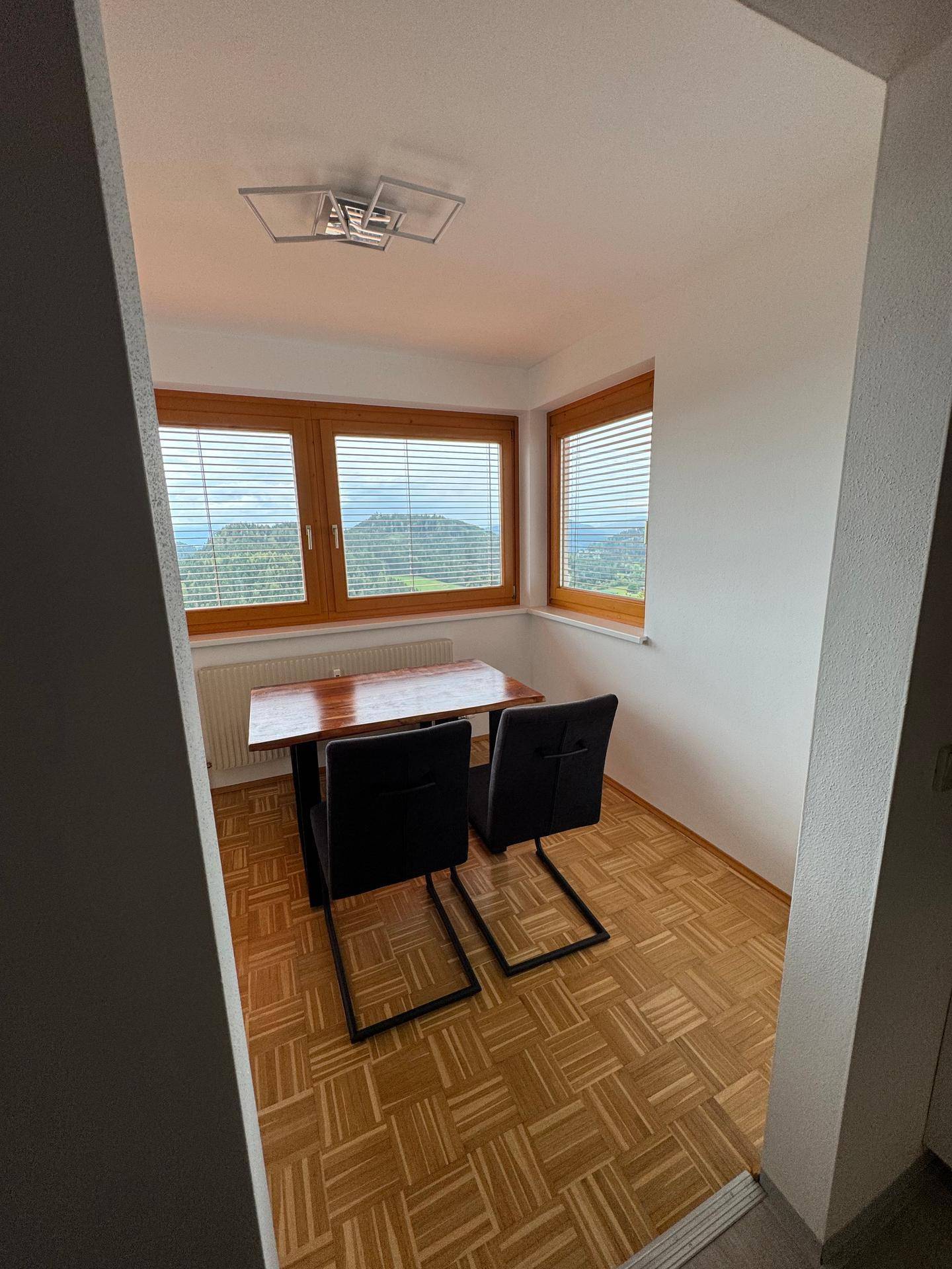 Gemütlicher Essbereich mit Holztisch, zwei Stühlen und weitem Blick in die Natur.