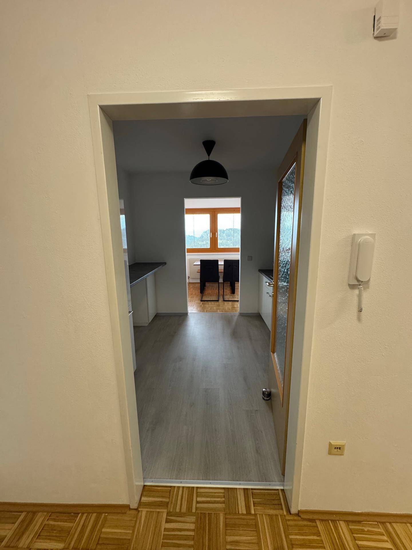 Blick durch eine Tür in eine helle Küche mit Fenster und Ausblick ins Grüne.