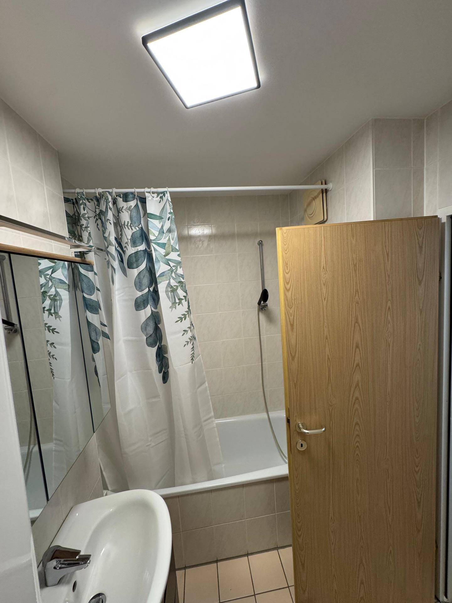 Badewanne mit Duschvorhang und hellen Wandfliesen in einem gepflegten Badezimmer.