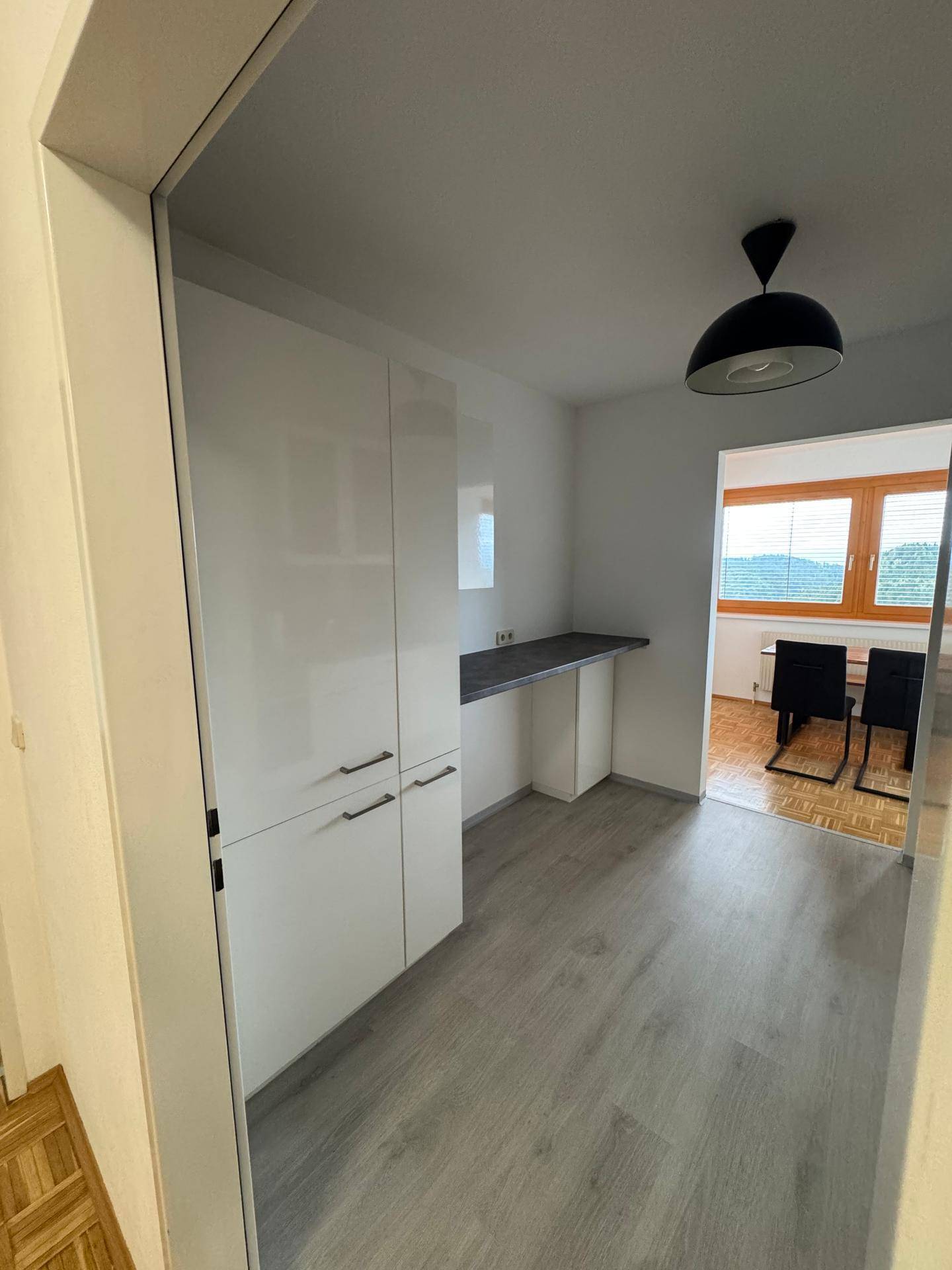 Moderne Küche mit weißen Schränken, grauer Arbeitsplatte und Blick in den Essbereich.