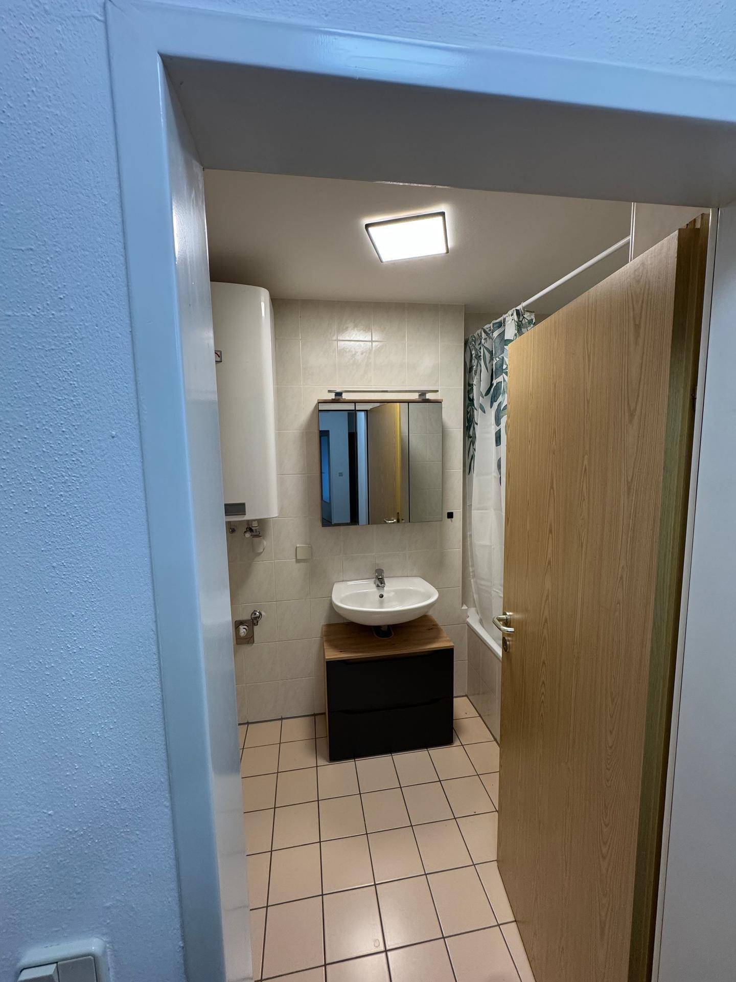 Funktionales Badezimmer mit hellen Fliesen, Waschbecken, Spiegelschrank und Badewanne mit Duschvorhang.