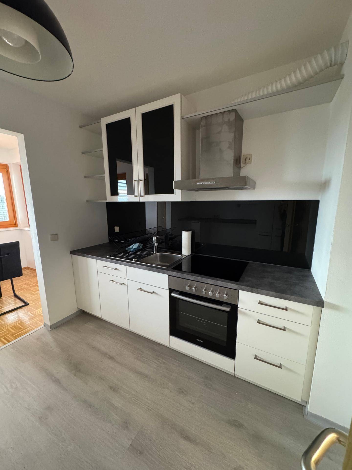 Funktionale Küche mit weißen Unterschränken, schwarzer Rückwand, Backofen und Induktionskochfeld.