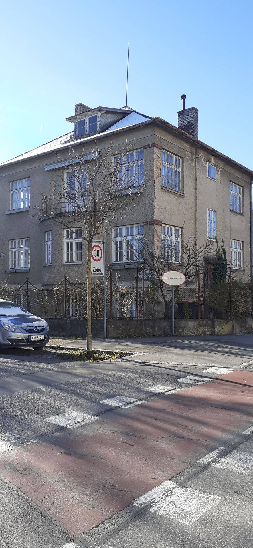 Eckansicht eines Mehrfamilienhauses mit traditioneller Architektur und Fenstern zur Straße.