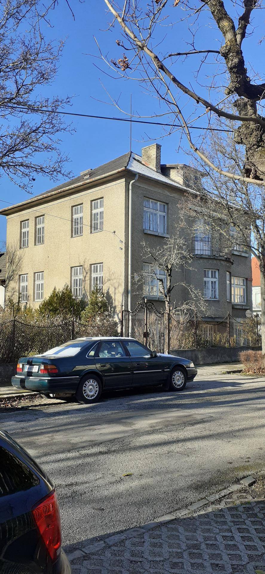 Seitenansicht eines älteren Wohnhauses mit mehreren Fenstern und einem gepflegten Vorgarten.