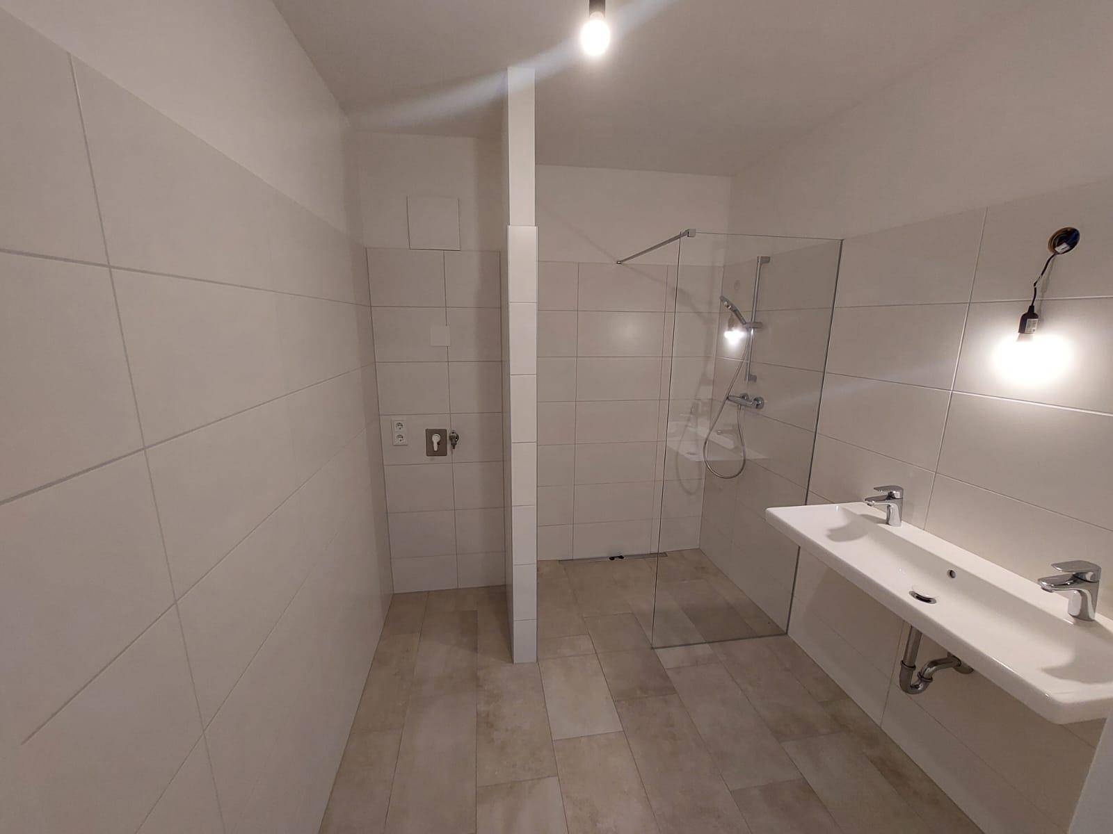 Modernes Badezimmer mit weißen Fliesen, einer begehbaren Dusche und einem Doppelwaschbecken.