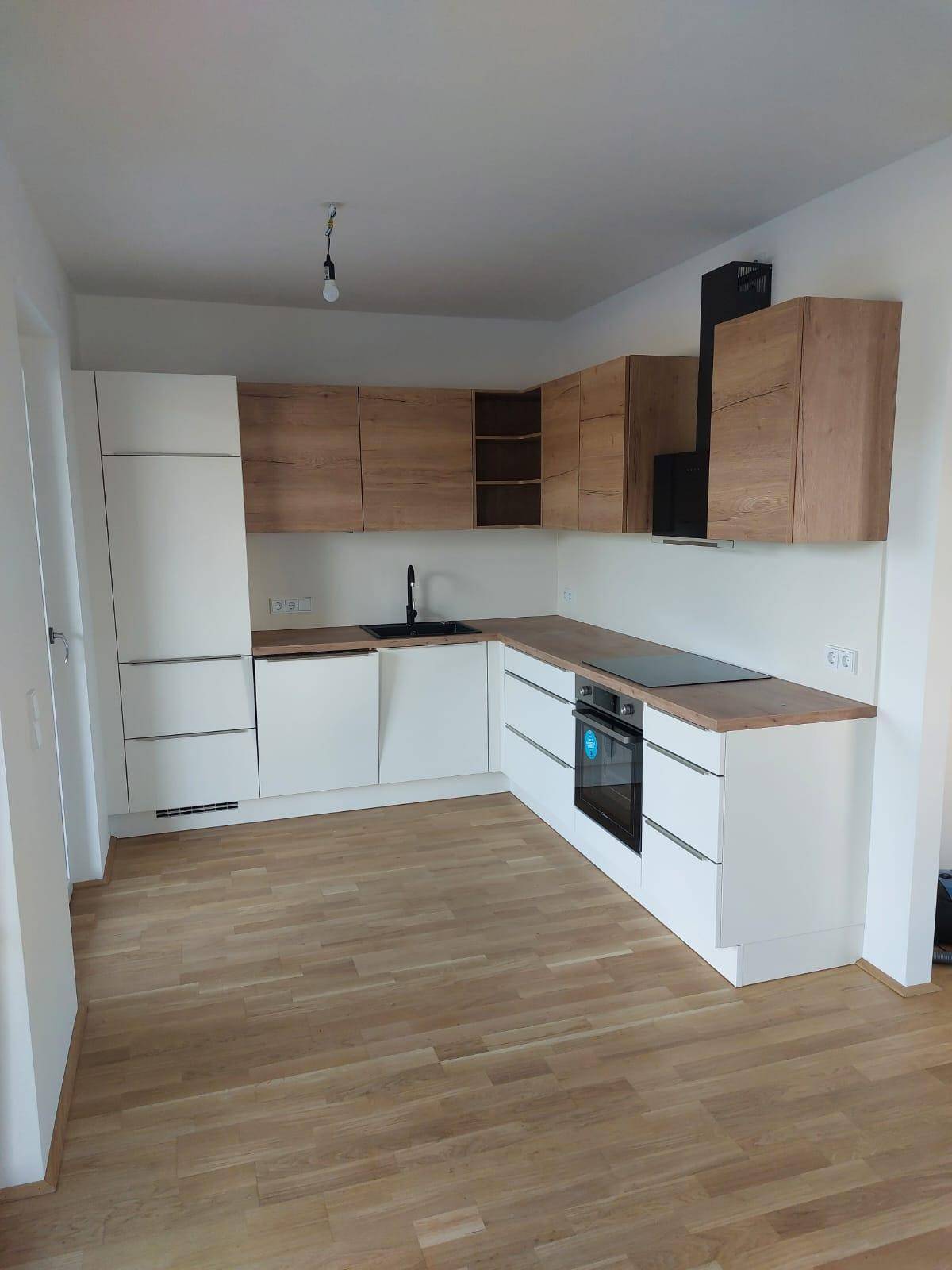 Geräumige L-förmige Küche mit weißen und holzfarbenen Schränken und Dunstabzugshaube.