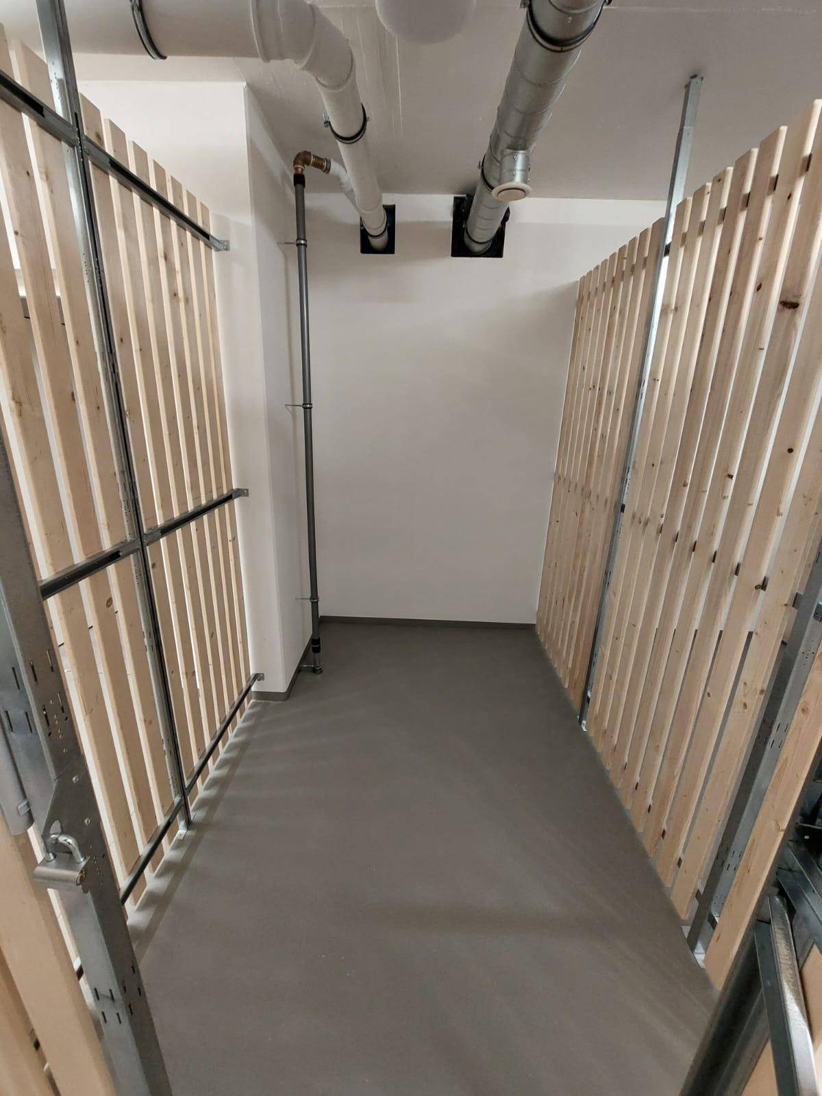 Kellerabteil mit Holzlattenwänden und sichtbaren Rohren an der Decke.