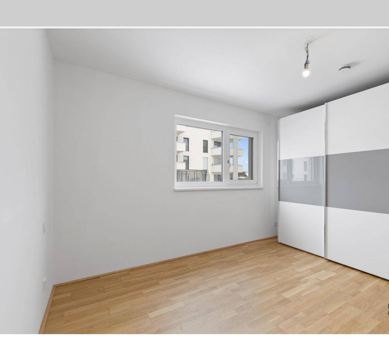 Schlafzimmer mit hellem Holzboden, großem Fenster und einem modernen Kleiderschrank.