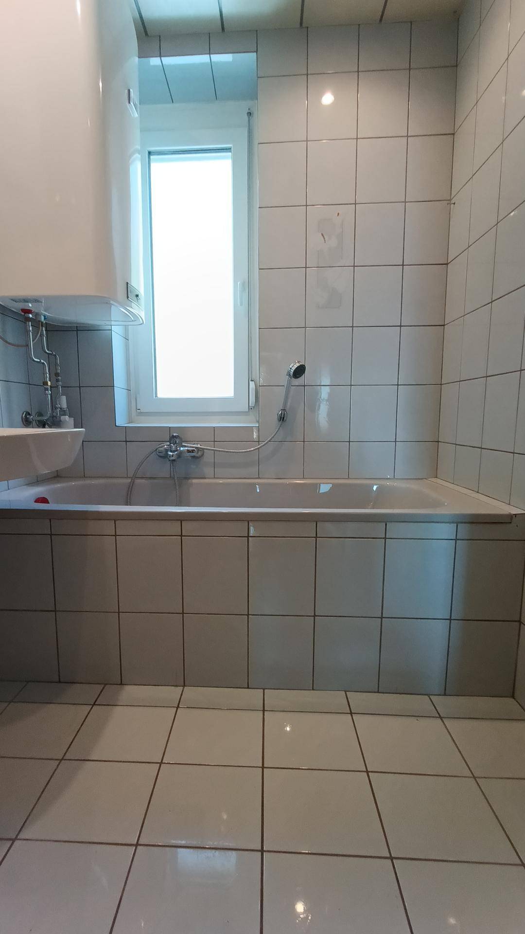 Gefliestes Badezimmer mit Badewanne, Duscharmatur und Fenster für Tageslicht.