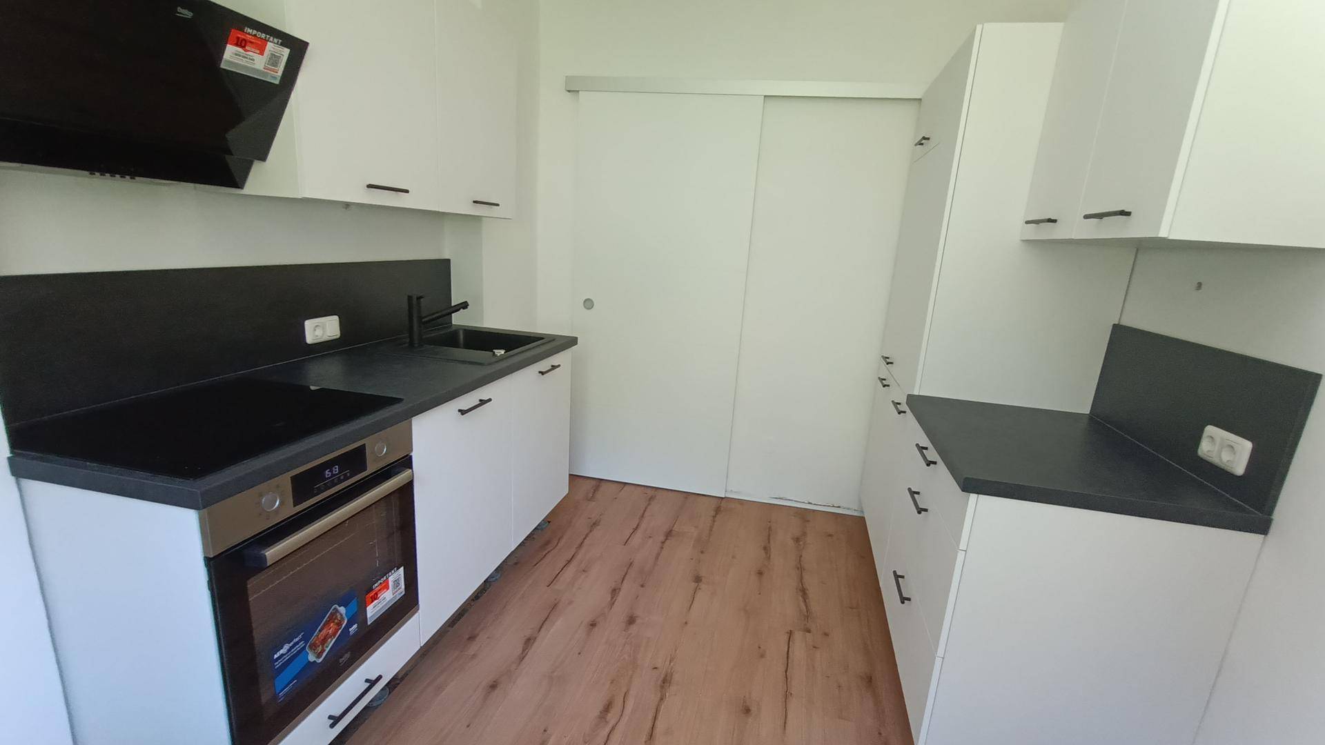 Moderne Küche mit weißen Schränken, dunkler Arbeitsplatte und integrierten Geräten.