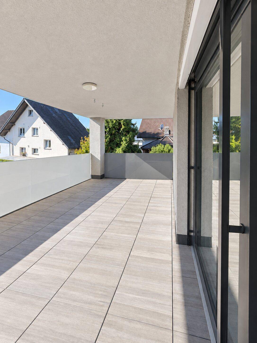 Geräumige, sonnige Terrasse mit Fliesenboden und Blick auf die umliegenden Häuser und Bäume.