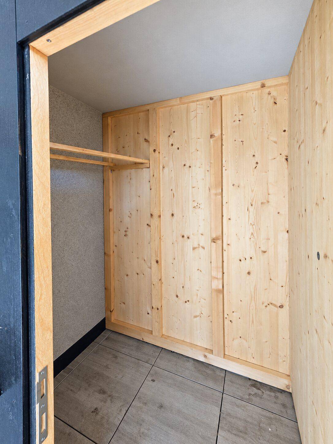 Praktischer Abstellraum mit Holzverkleidung, Regalen und Kleiderstange, zugänglich von der Terrasse.