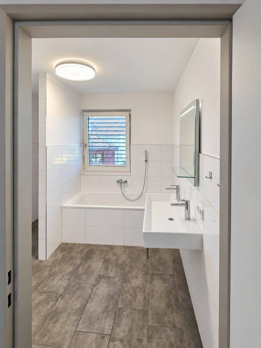 Modernes Badezimmer mit Badewanne, Einzelwaschbecken, Spiegel und Fenster mit Jalousien.