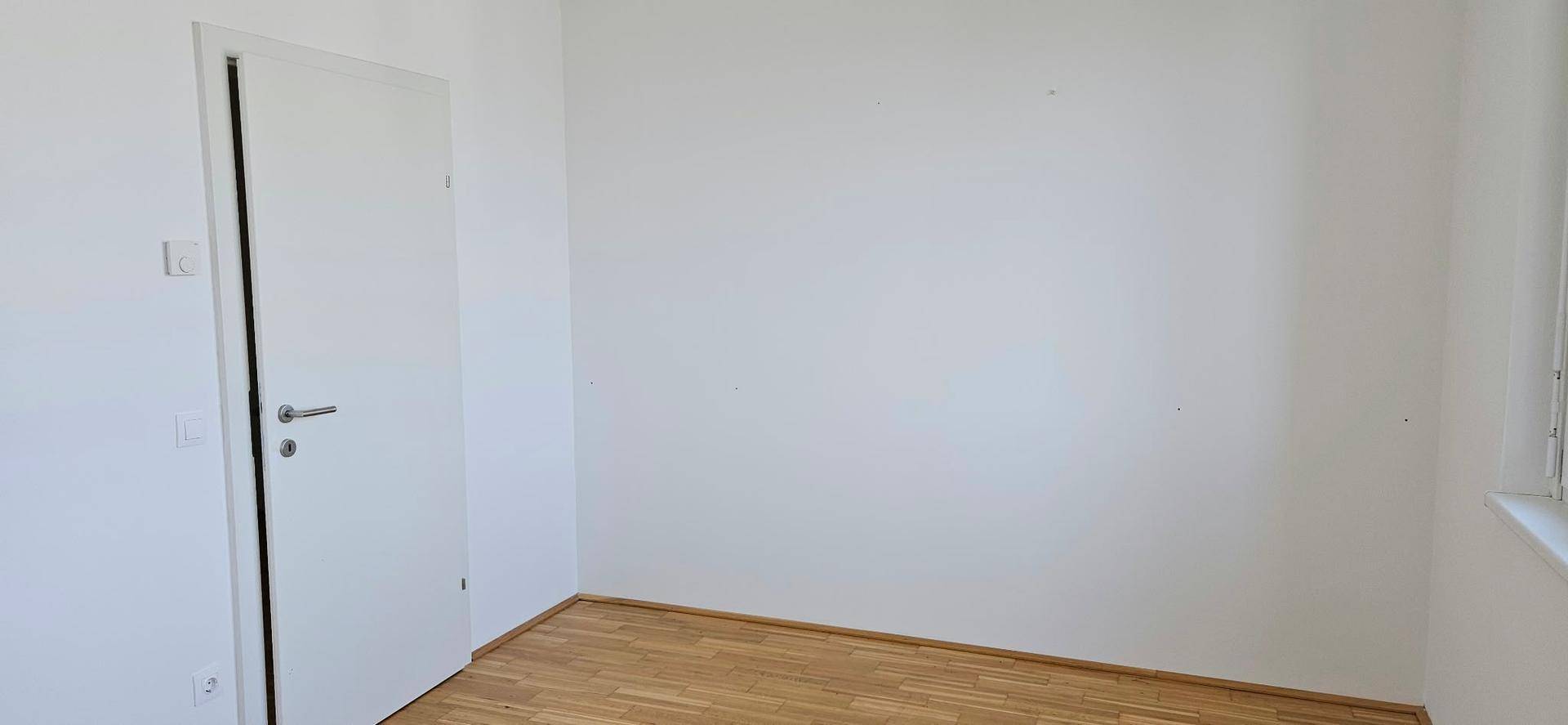 Schlafzimmer mit Holzboden und weiß gestrichenen Wänden, bereit zur individuellen Gestaltung.