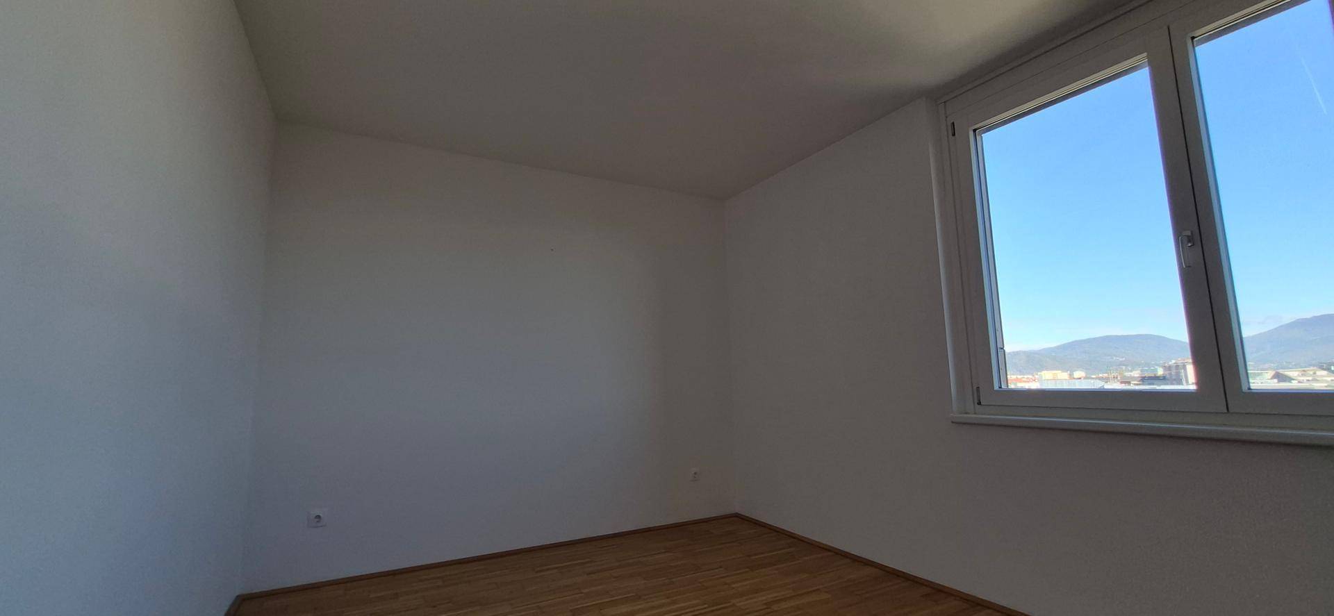 Schlafzimmer mit Holzboden und großem Fenster, das viel Tageslicht hereinlässt.