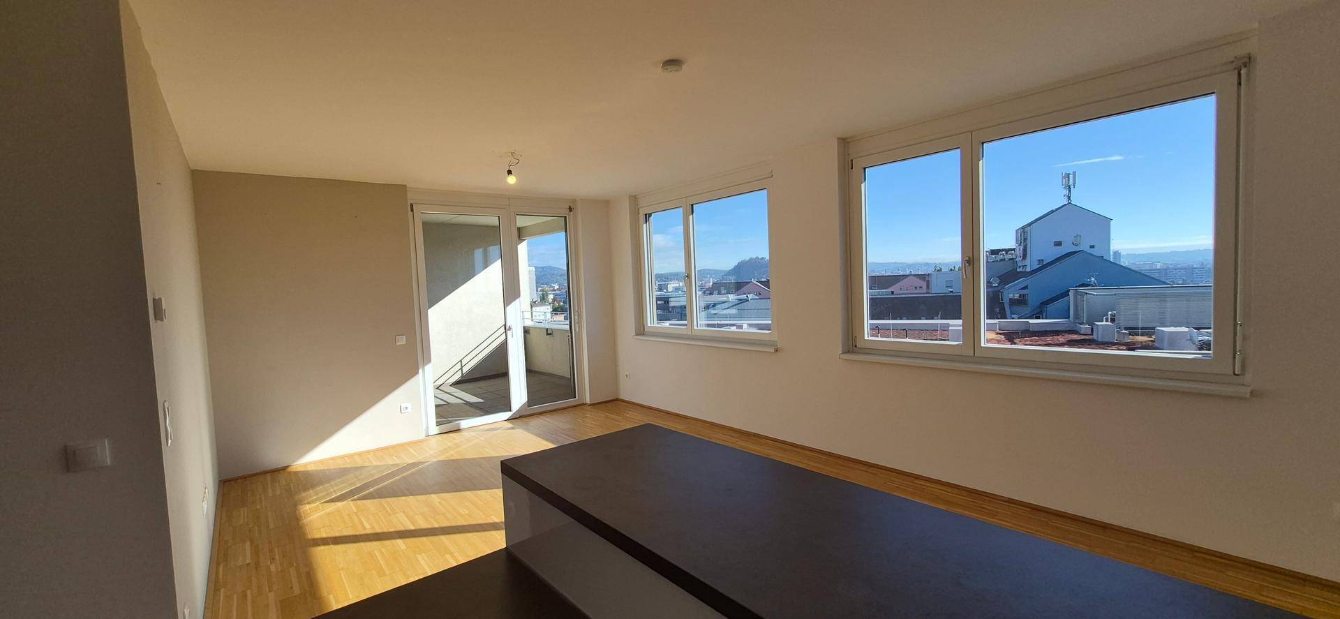 Heller Wohnbereich mit Holzboden, großen Fenstern und Zugang zum Balkon.