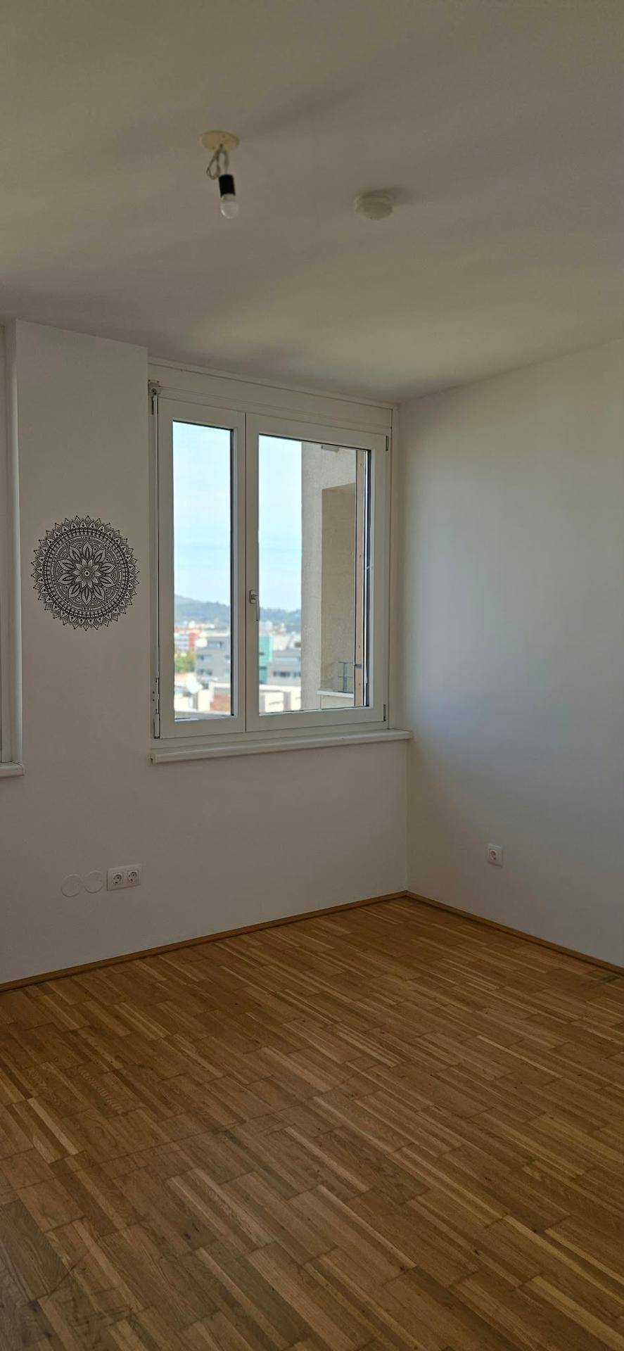 Helles Schlafzimmer mit Holzboden und Fenster mit Blick auf die Umgebung.