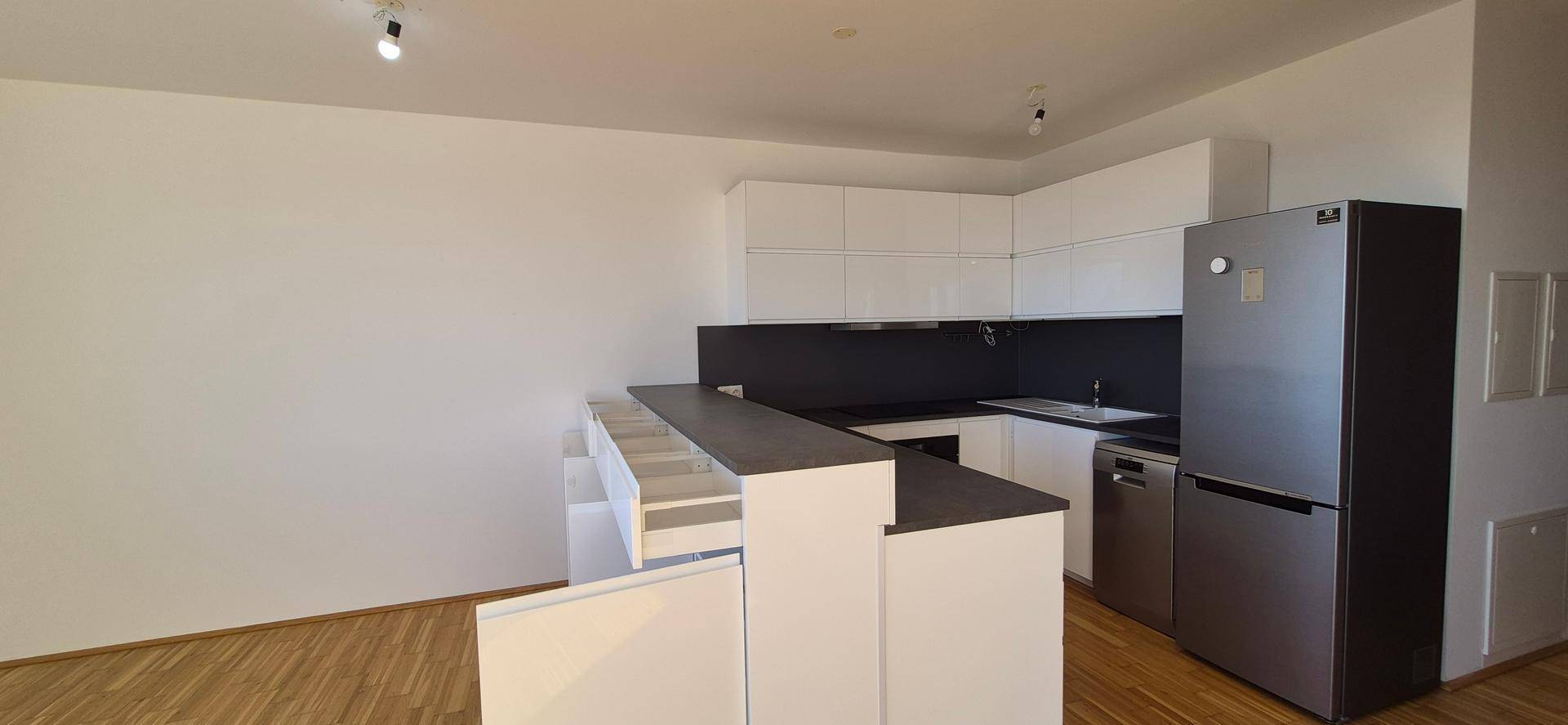 Moderne Einbauküche mit weißen Schränken, dunkler Arbeitsplatte und Kühlschrank.