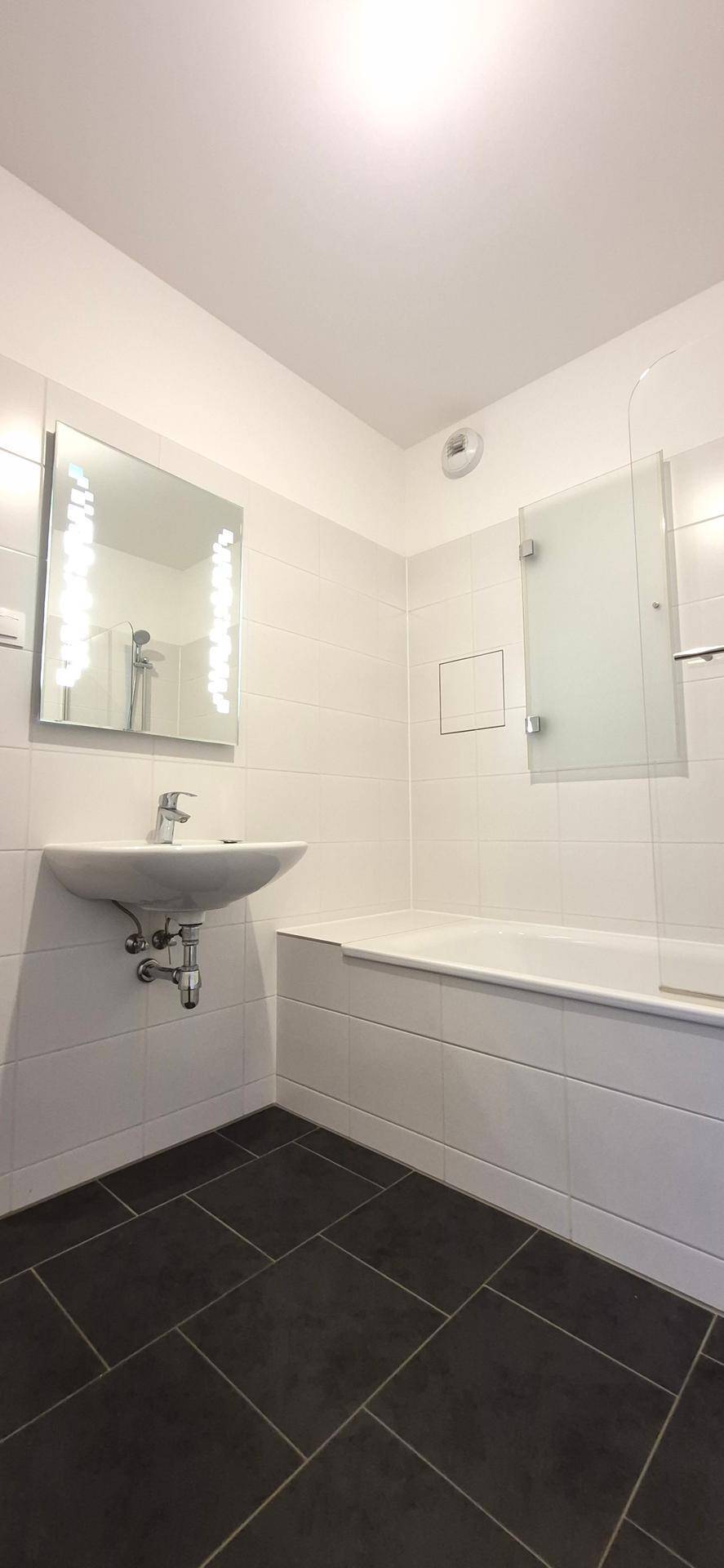 Badezimmer mit Badewanne, Waschbecken und dunklen Bodenfliesen für einen Kontrast.