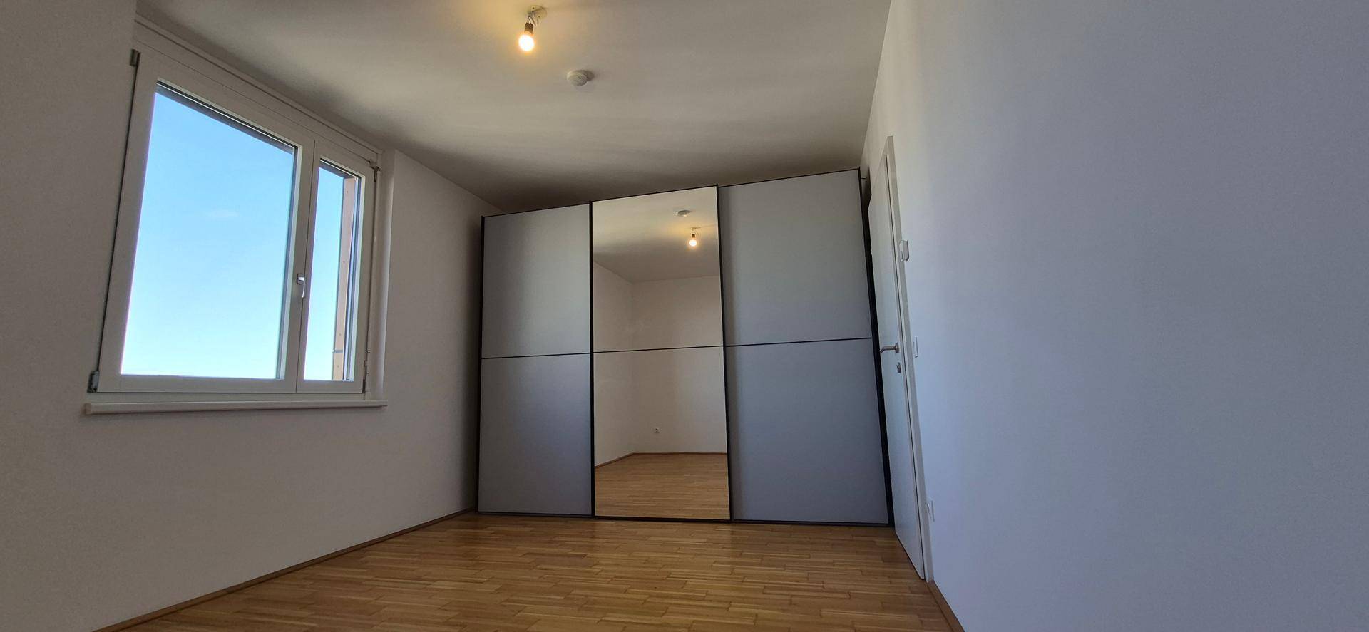 Schlafzimmer mit Holzboden und einem großen Spiegelschrank, der den Raum erweitert.