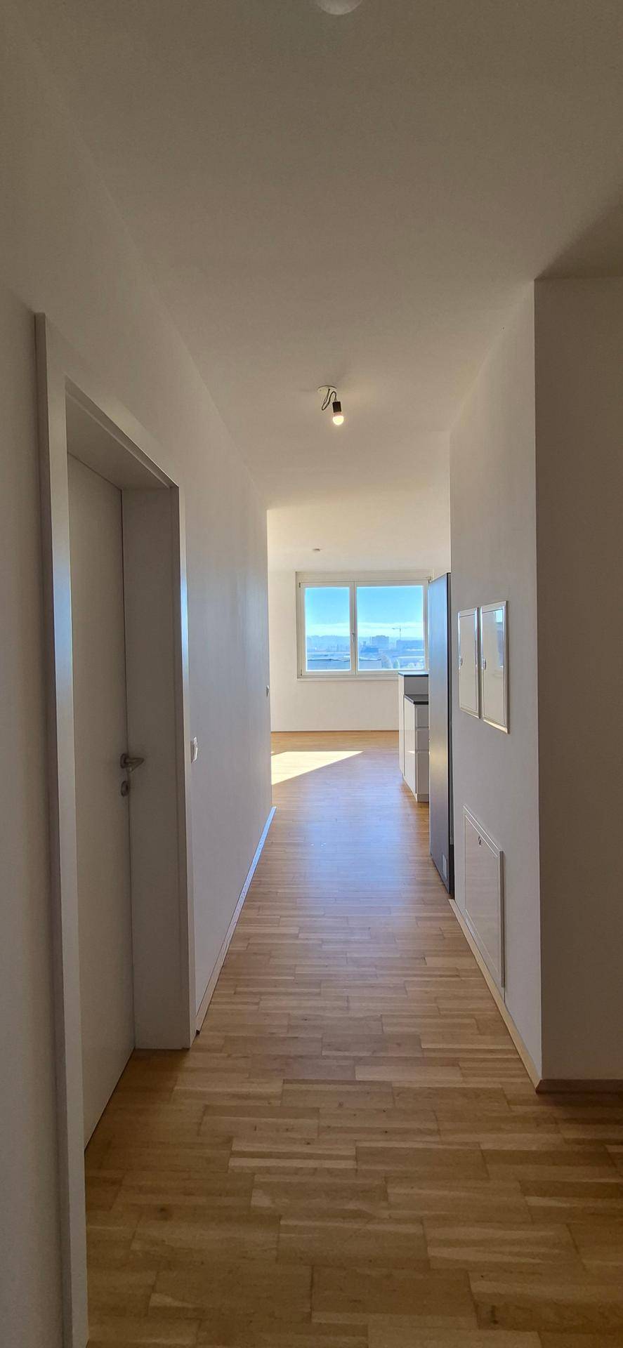 Heller Flur mit Holzboden und Blick auf die Fensterfront am Ende.
