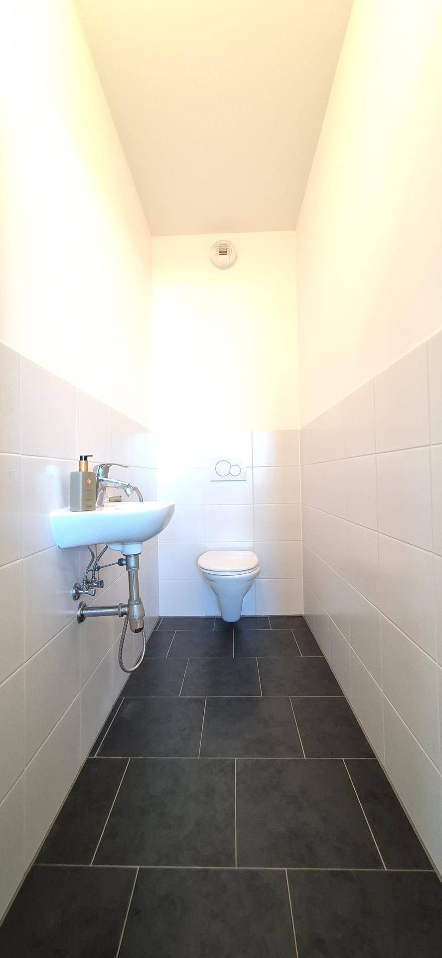 Separates Gäste-WC mit Waschbecken und Toilette, ausgestattet mit dunklen Bodenfliesen.