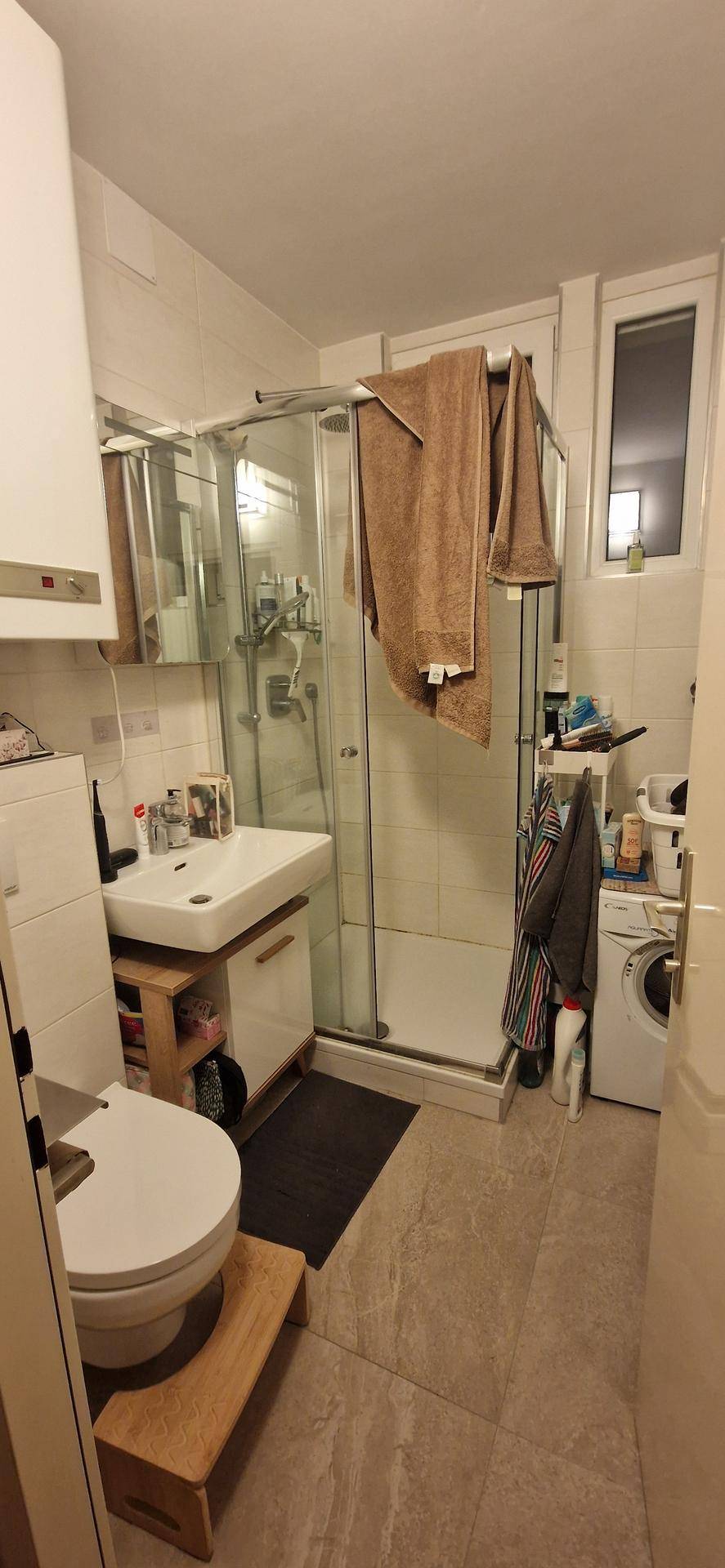 Badezimmer mit Duschkabine, WC, Waschbecken und Waschmaschine, ausgestattet mit einem Fenster.