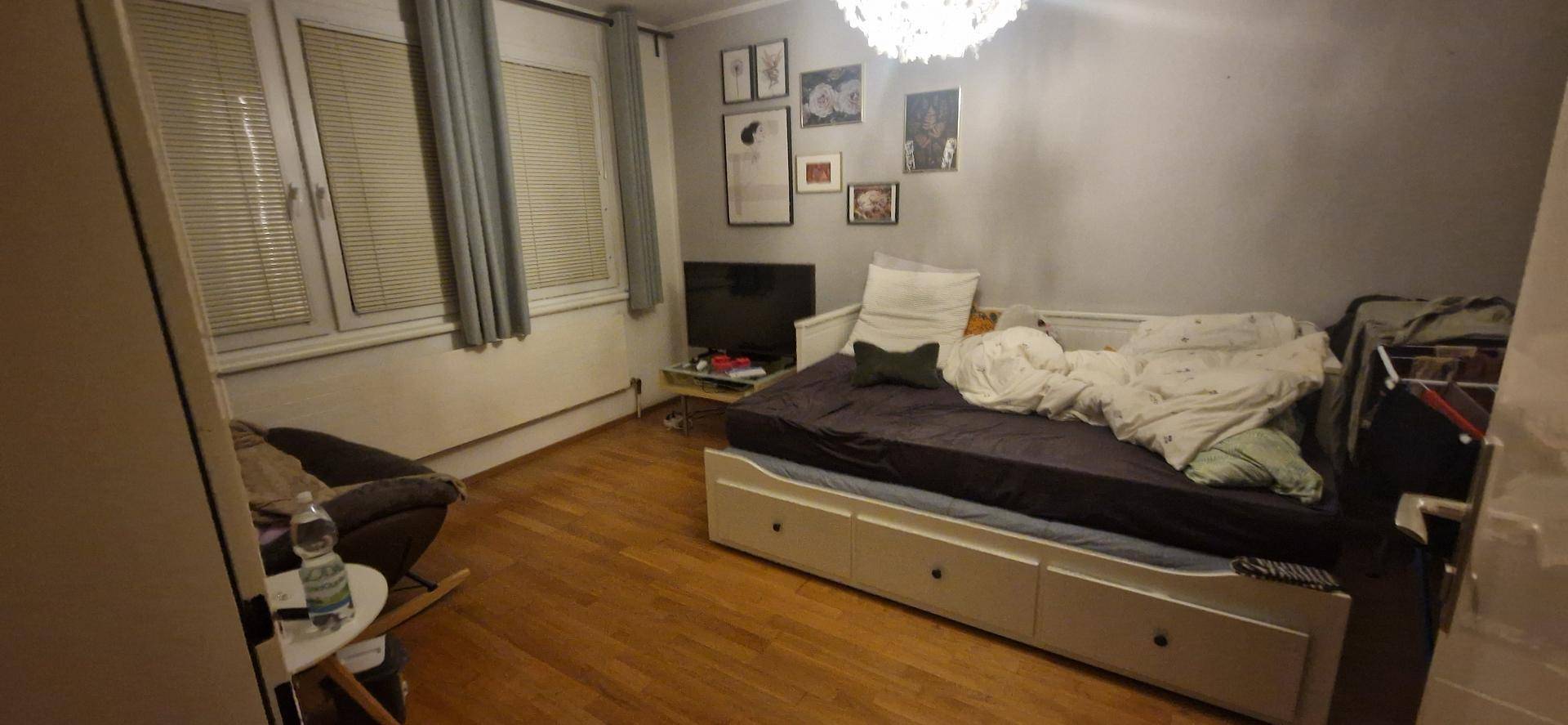 Gemütliches Schlafzimmer mit Holzboden, Bett mit Stauraum und kleiner Sitzecke am Fenster.