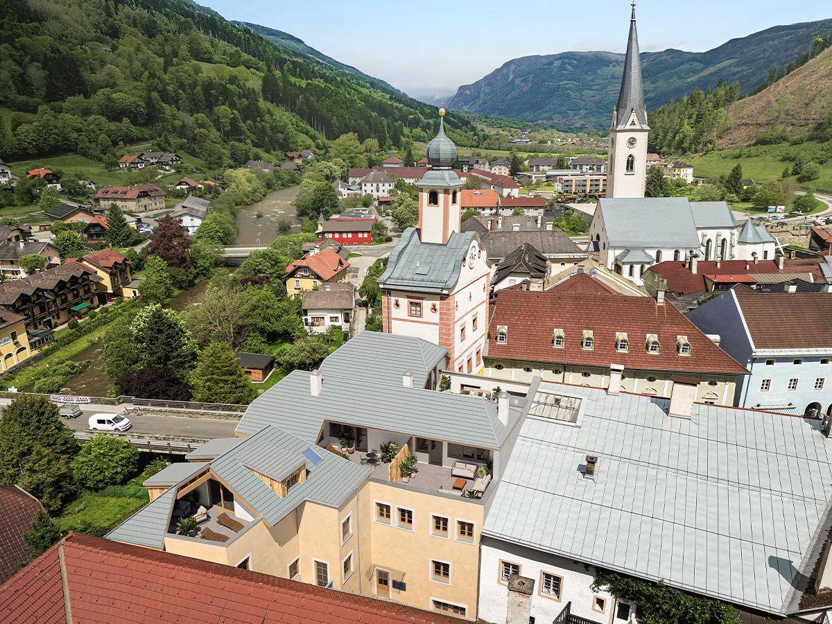 Luftaufnahme einer malerischen Stadt im Tal mit Fluss, traditionellen Gebäuden und umliegenden grünen Bergen.
